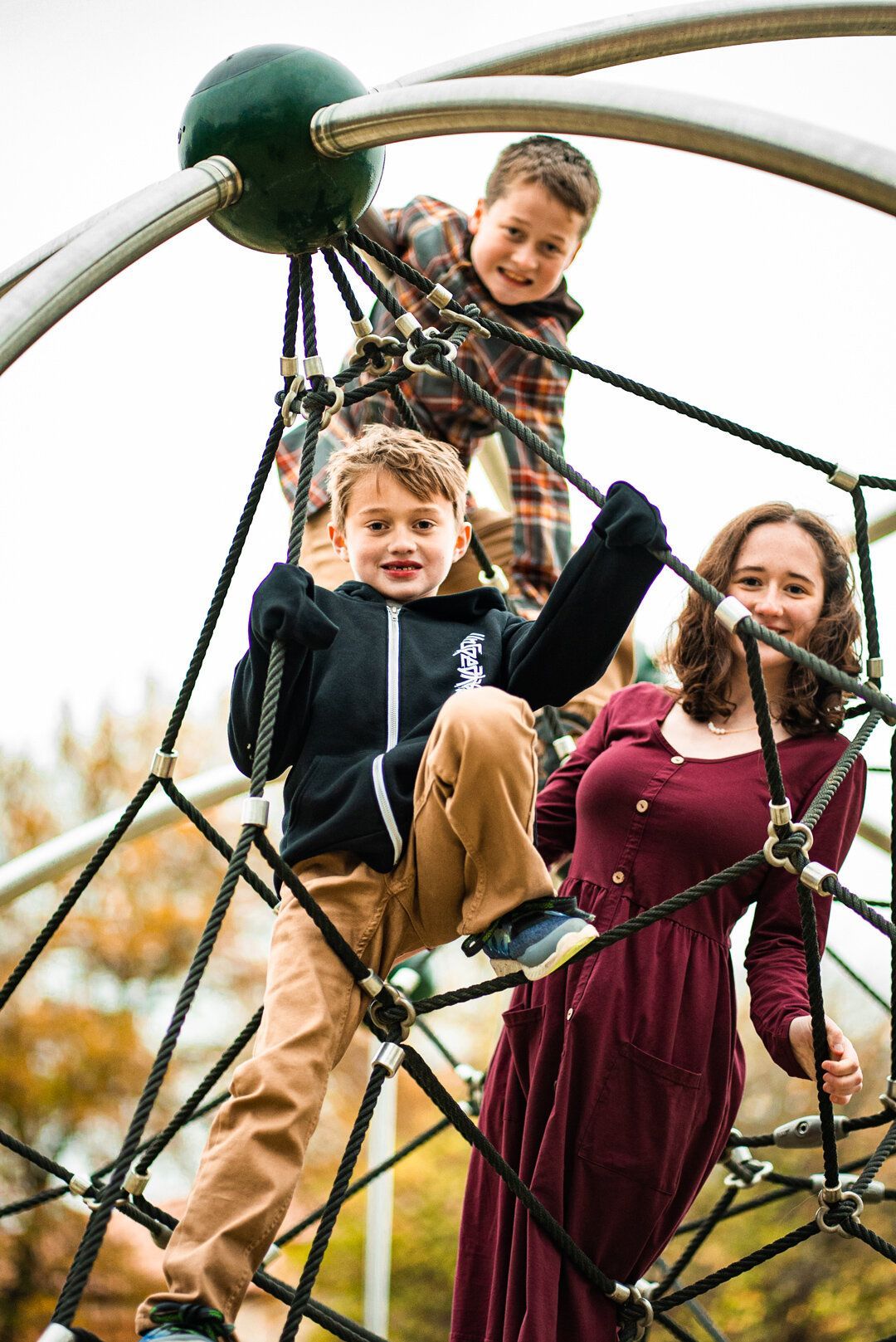 A woman and two children are playing on a ropes course at a playground.