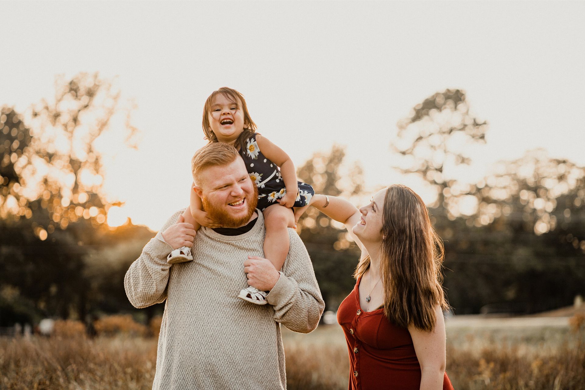 A man is carrying a little girl on his shoulders in a field.