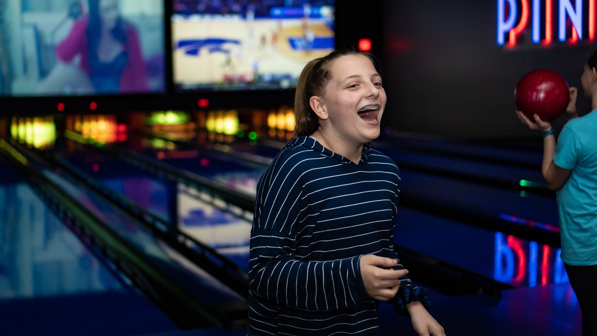 A young girl is laughing while bowling on a bowling alley.