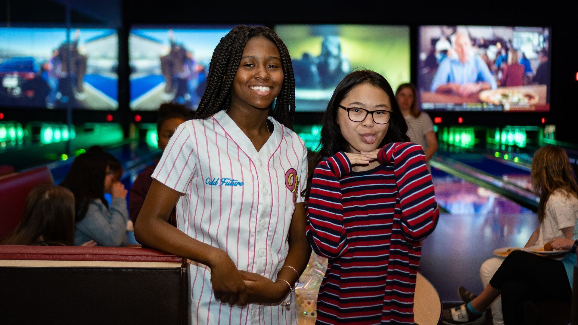 Two young women are posing for a picture in a bowling alley.
