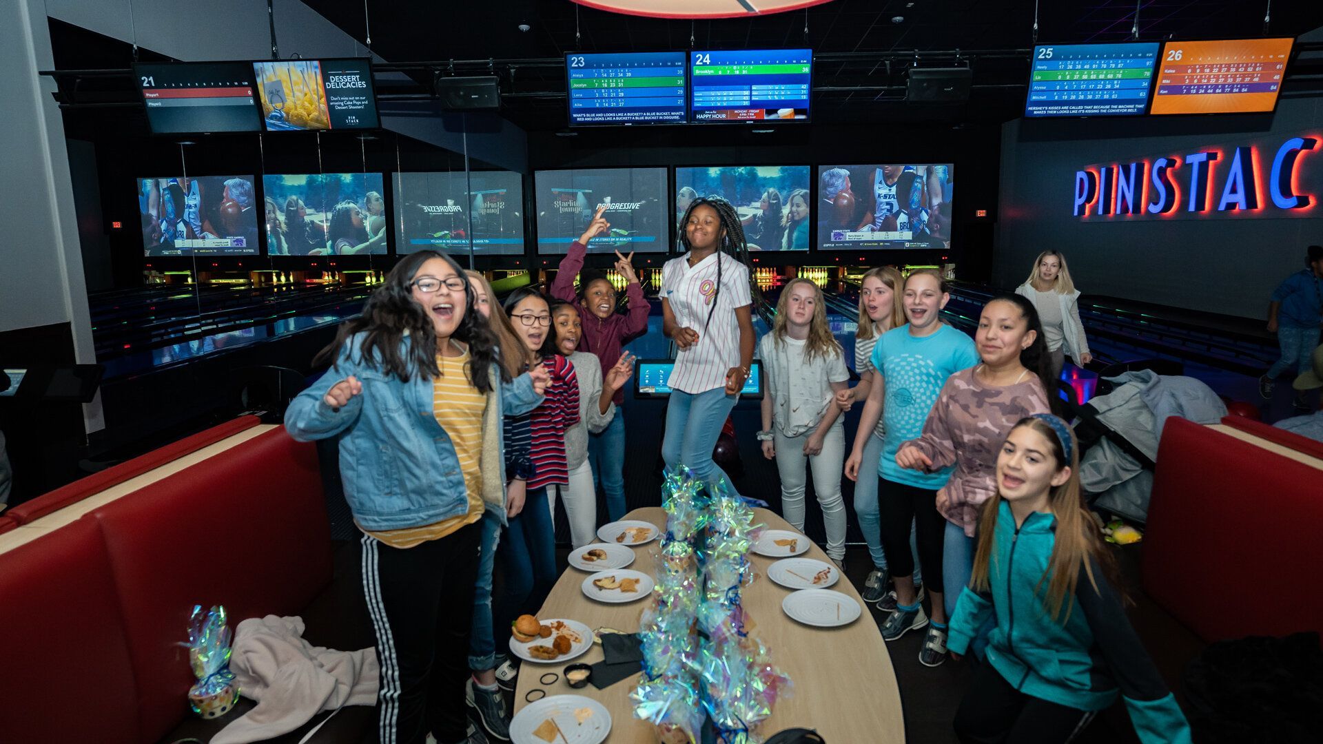 A group of young girls are standing around a table in a bowling alley.