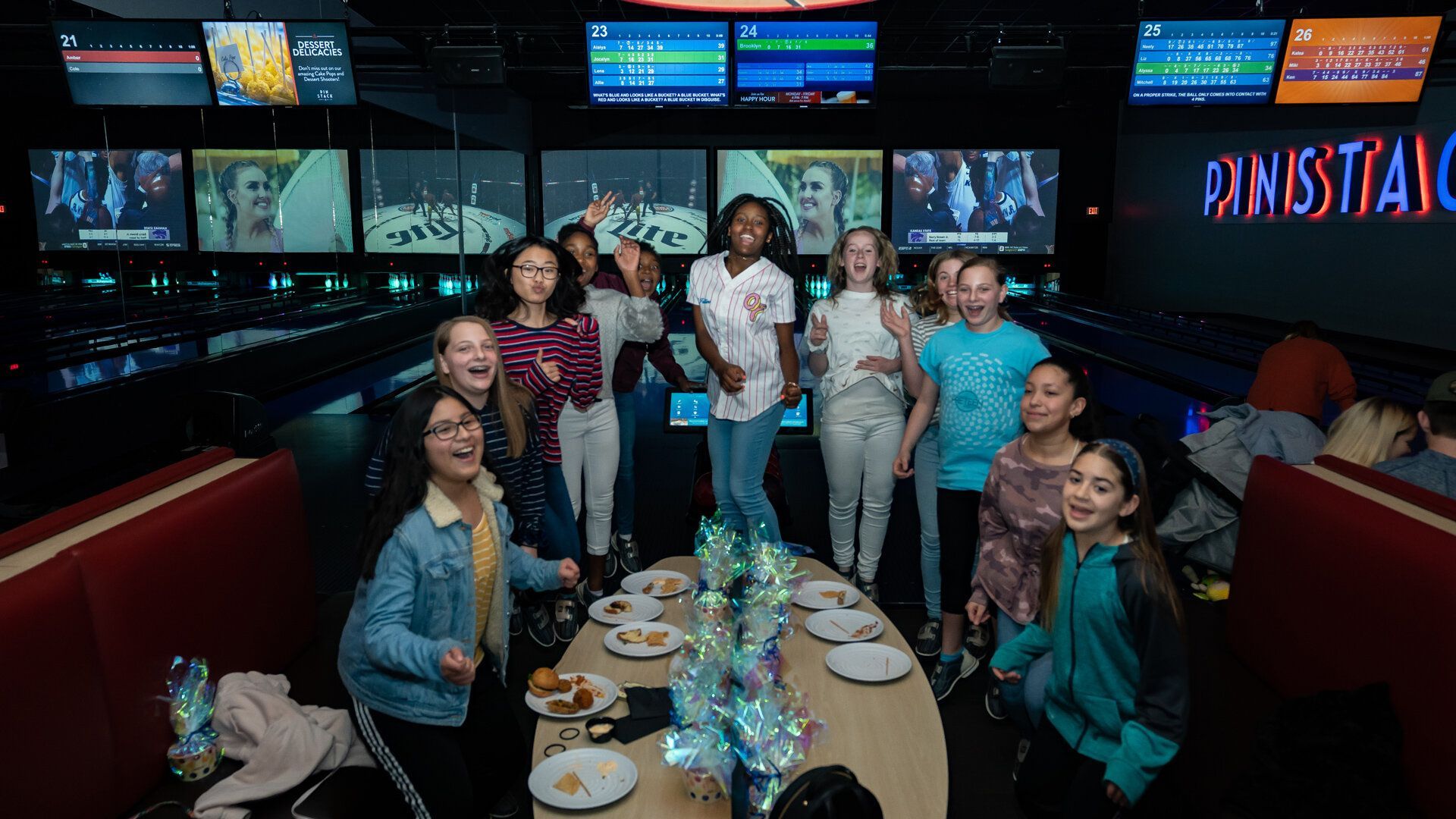 A group of young girls are sitting around a table in a bowling alley.