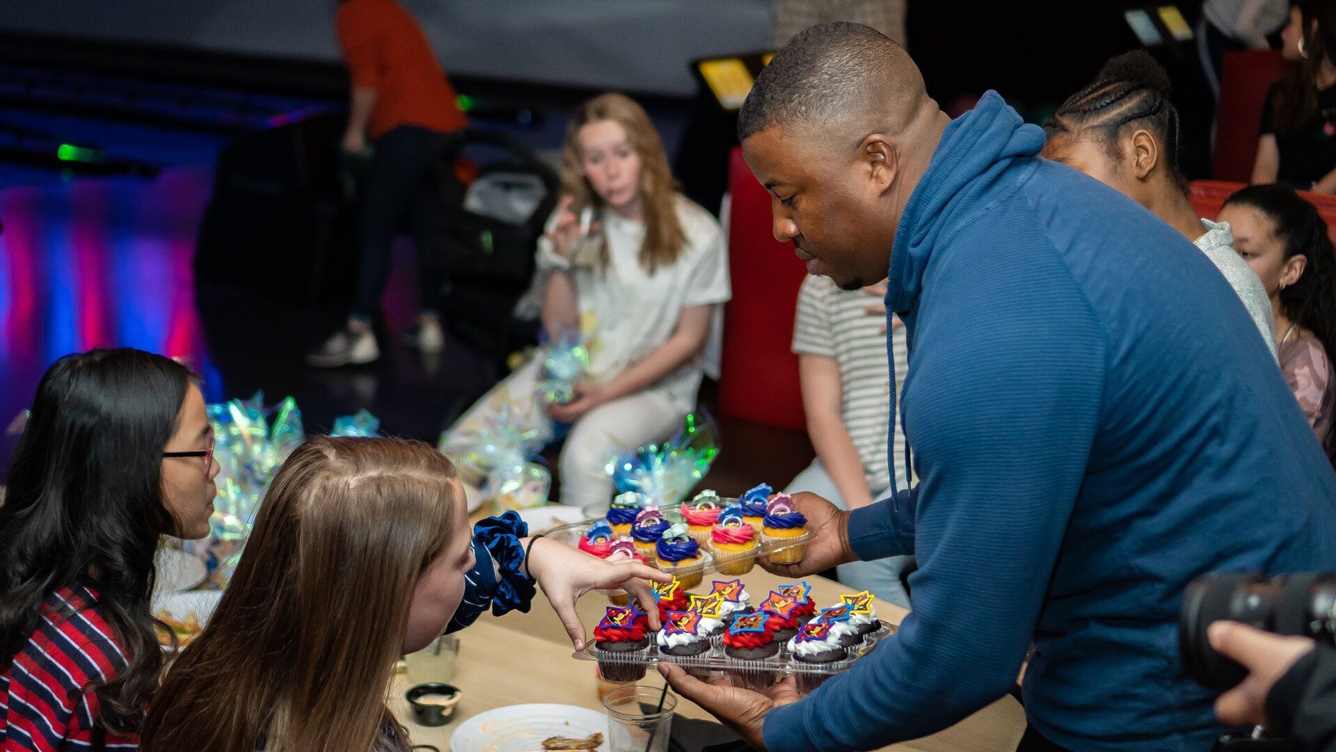 A man is serving cupcakes to a group of people at a party.