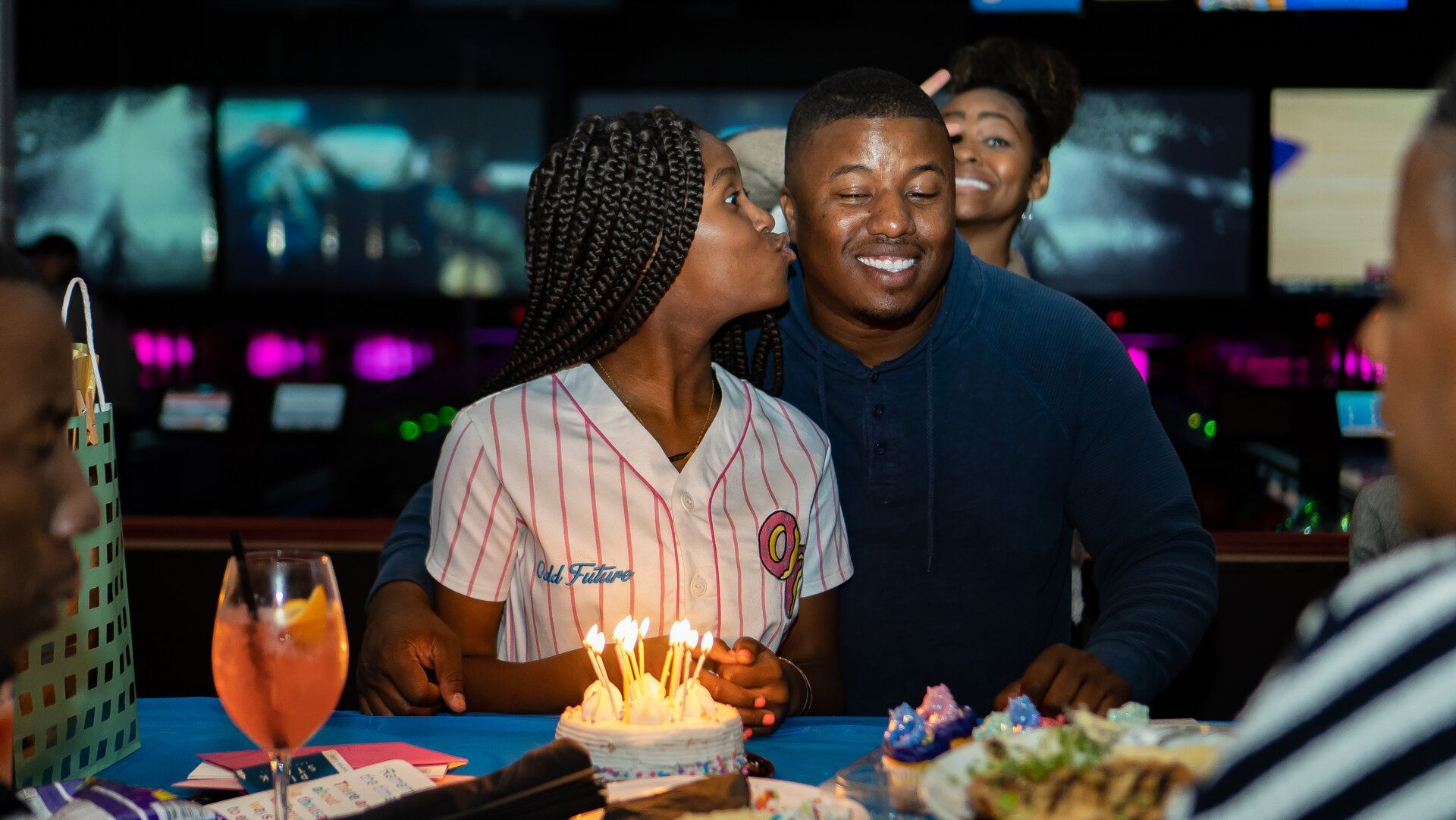 A woman is kissing a man on the cheek while holding a birthday cake with candles.