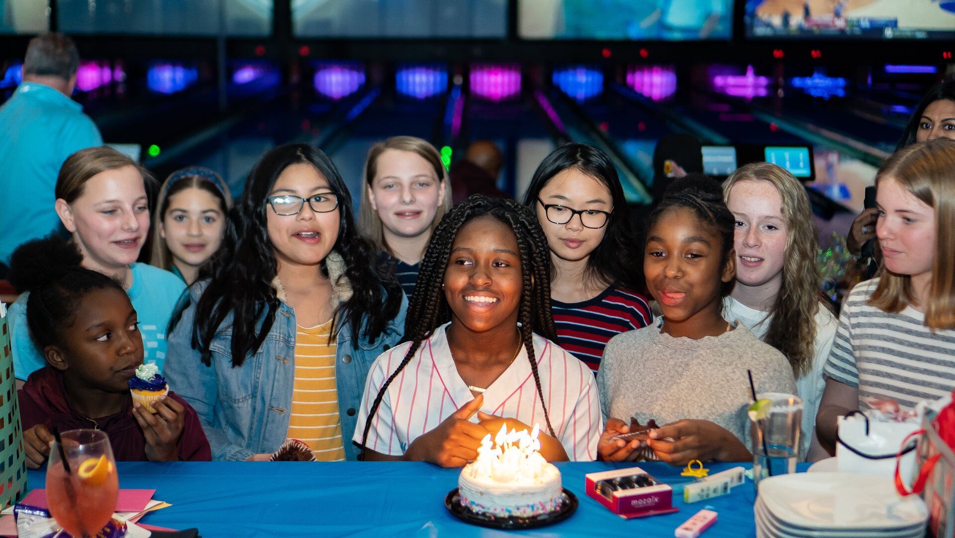 A group of young girls are celebrating a birthday at a bowling alley.