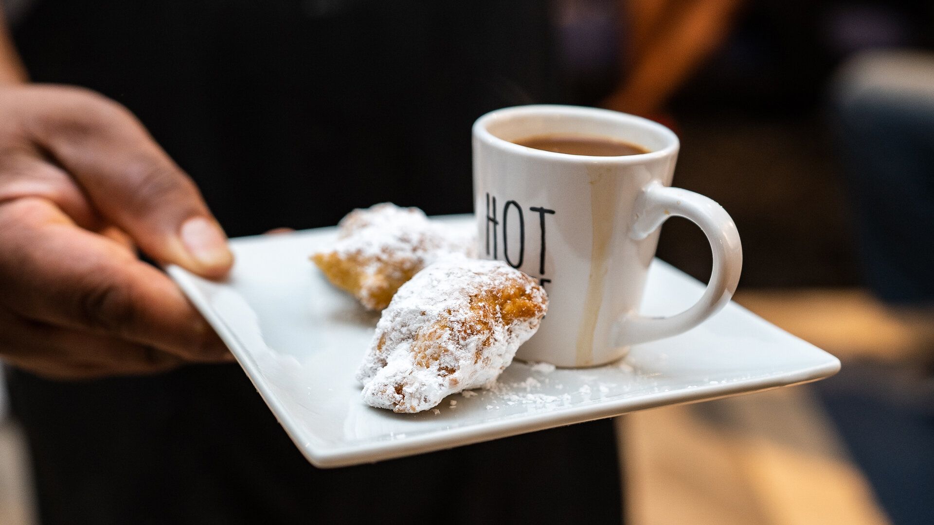 A person is holding a plate of food and a cup of coffee.