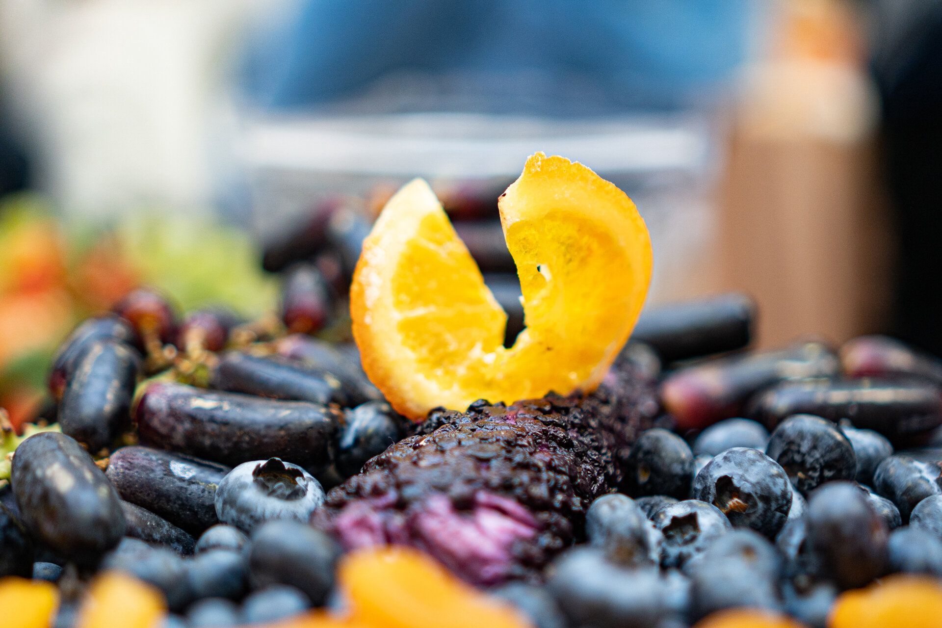 A slice of orange is sitting on top of a pile of blueberries.