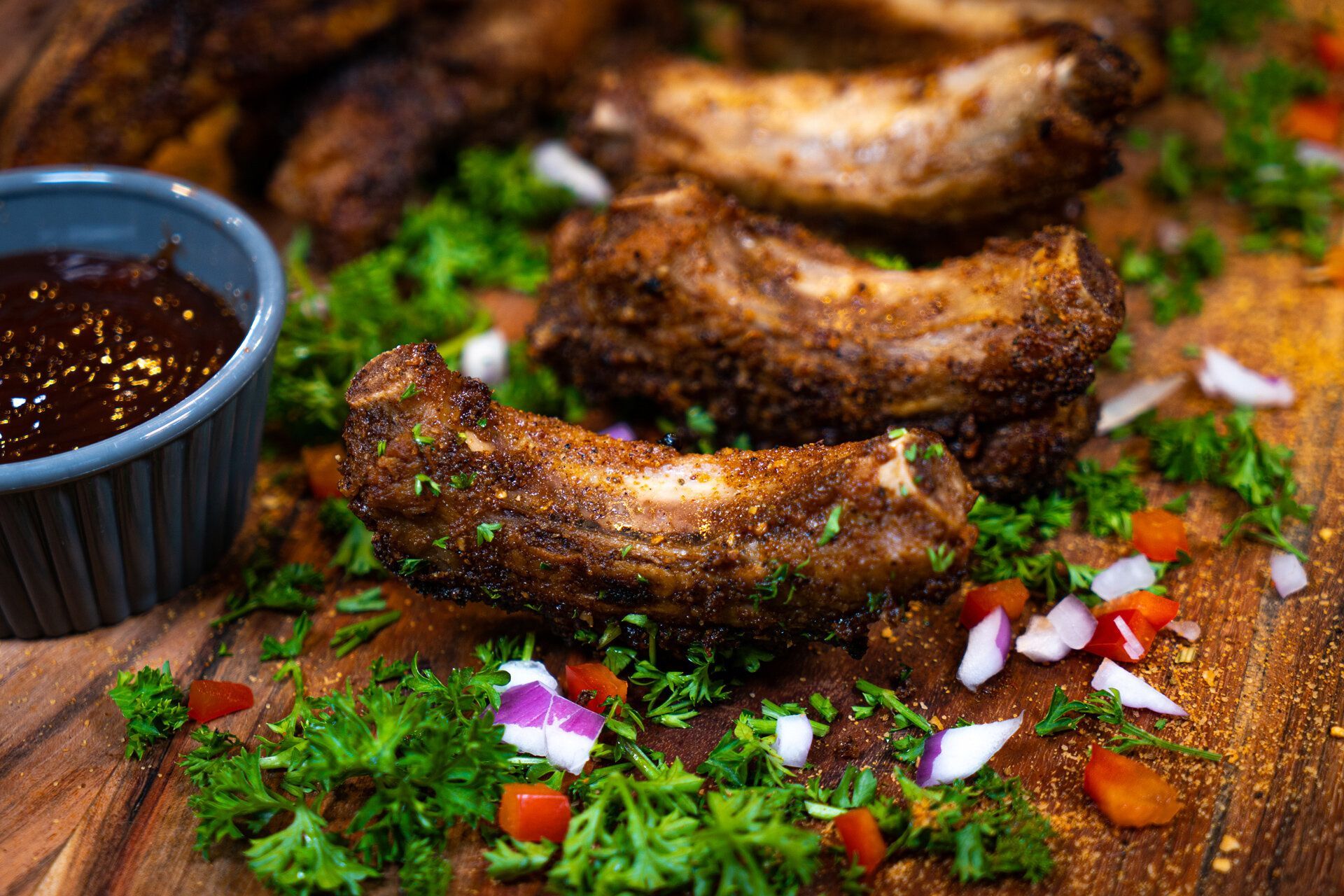 A wooden cutting board topped with ribs and a bowl of sauce.