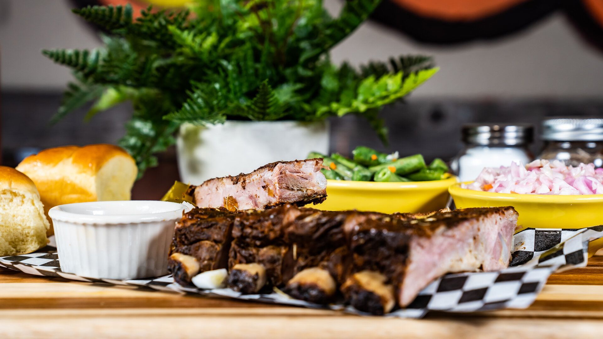 A tray of ribs and green beans on a wooden table.
