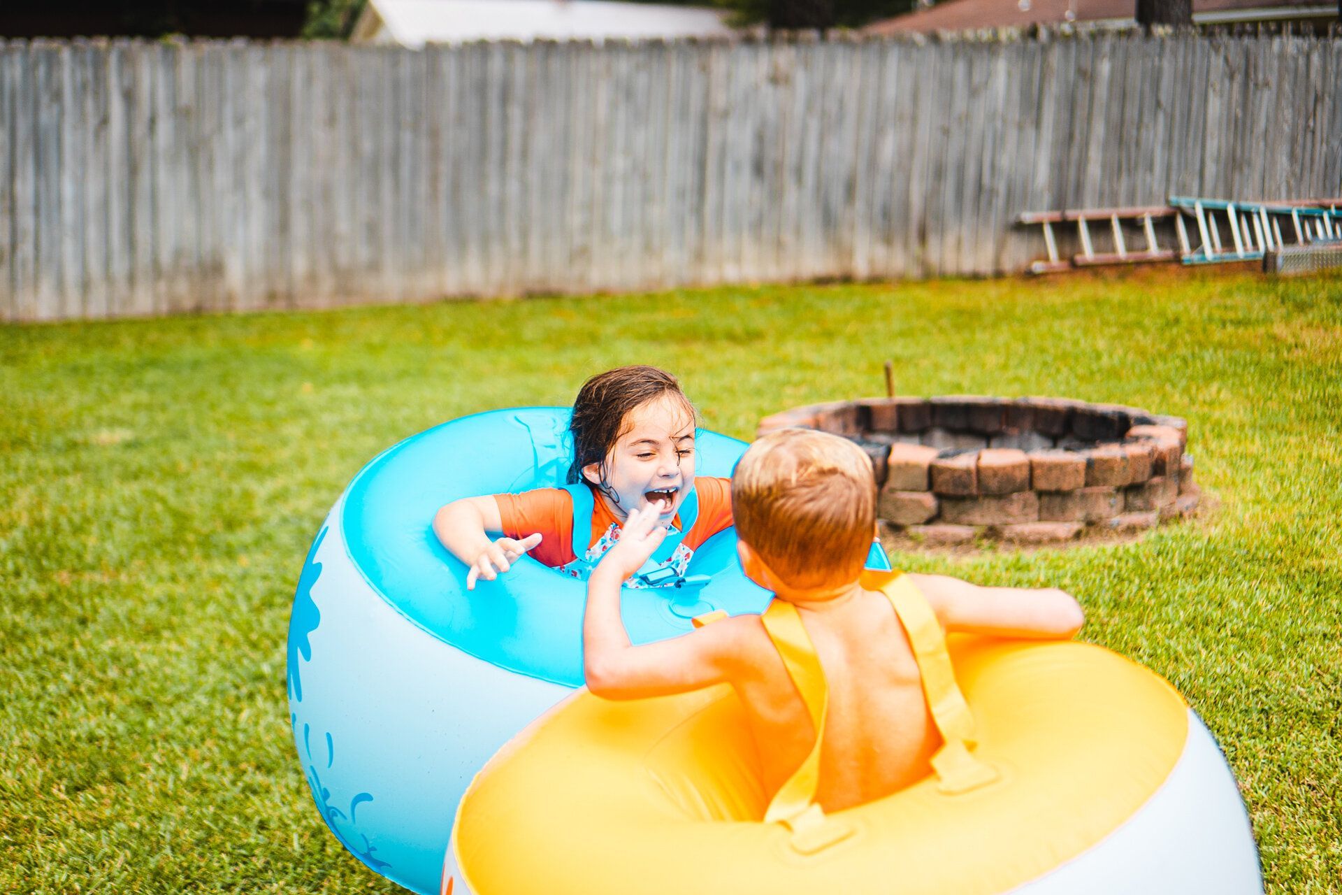 A boy and a girl are playing in an inflatable pool in a backyard.