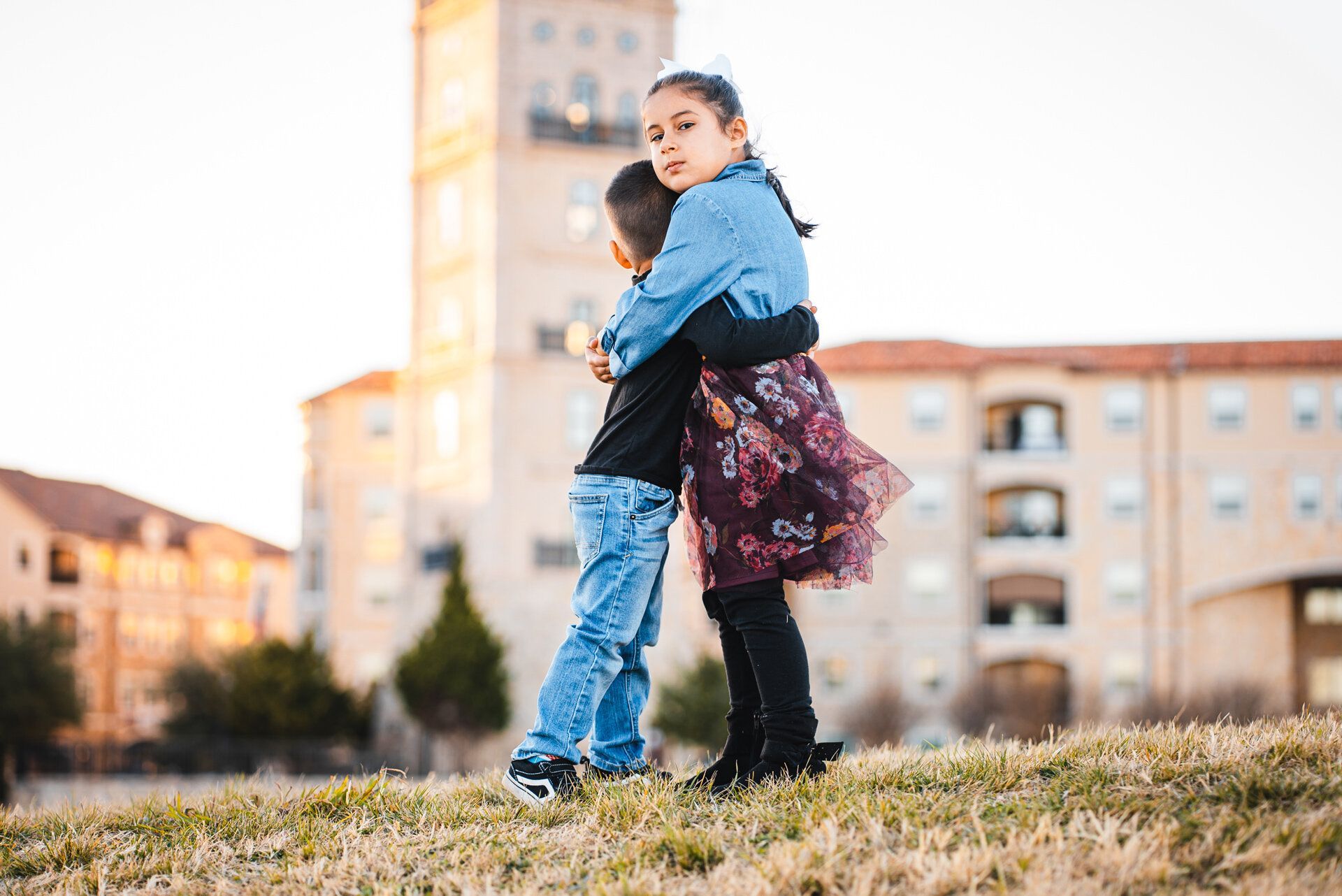 A boy and a girl are hugging each other in front of a building.