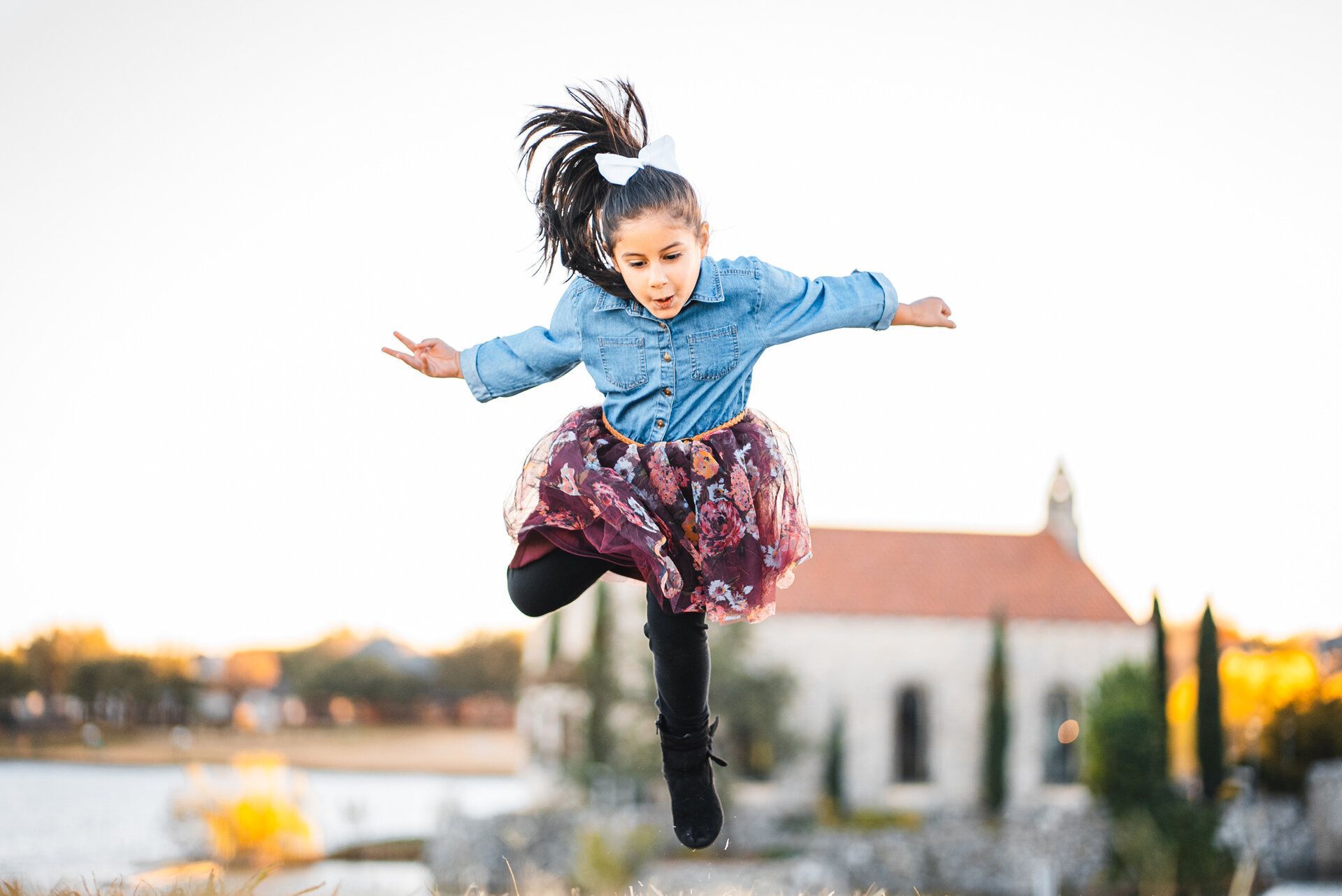 A little girl is jumping in the air with her arms outstretched.