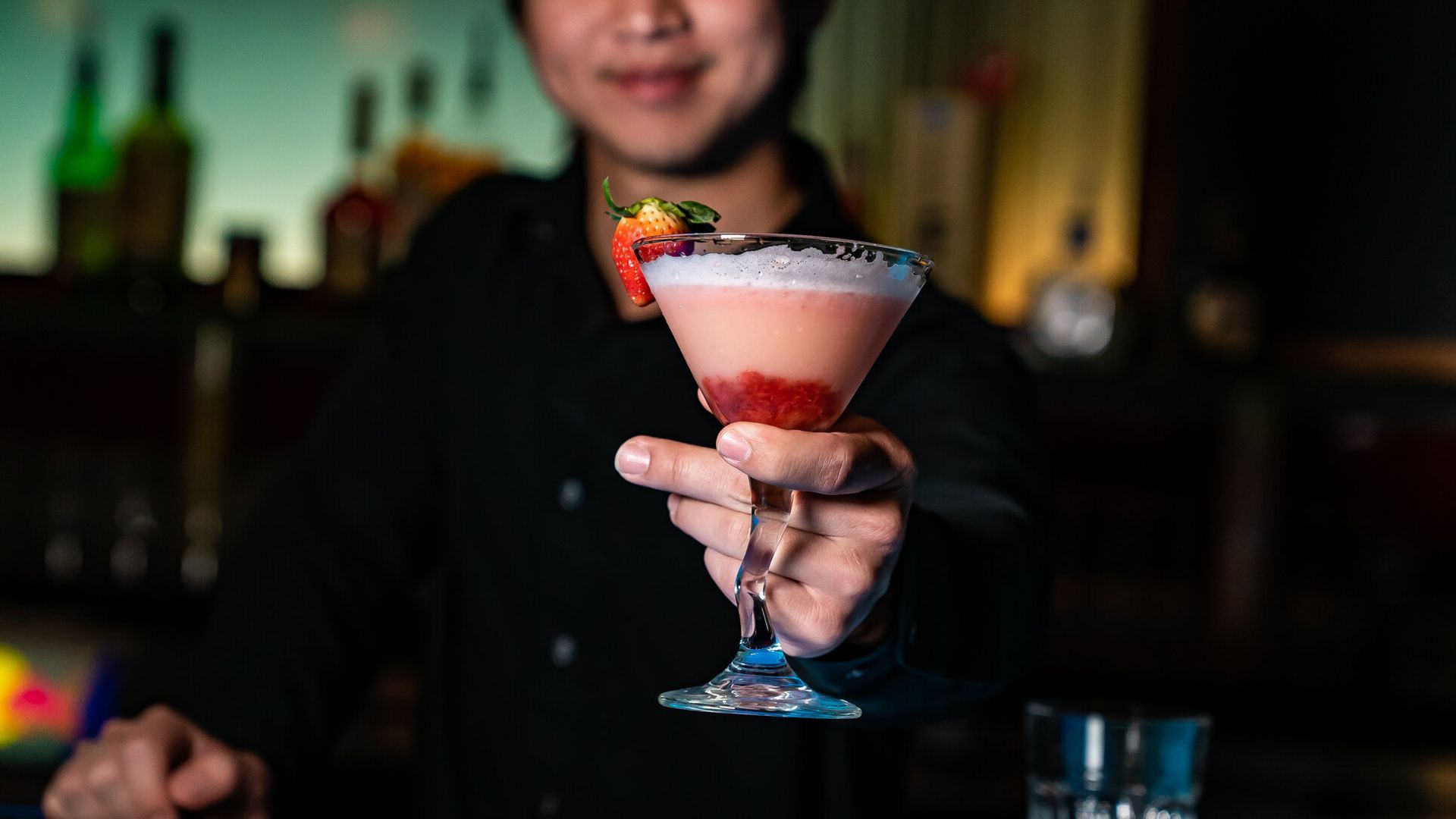 A bartender is holding a martini with strawberries in it.