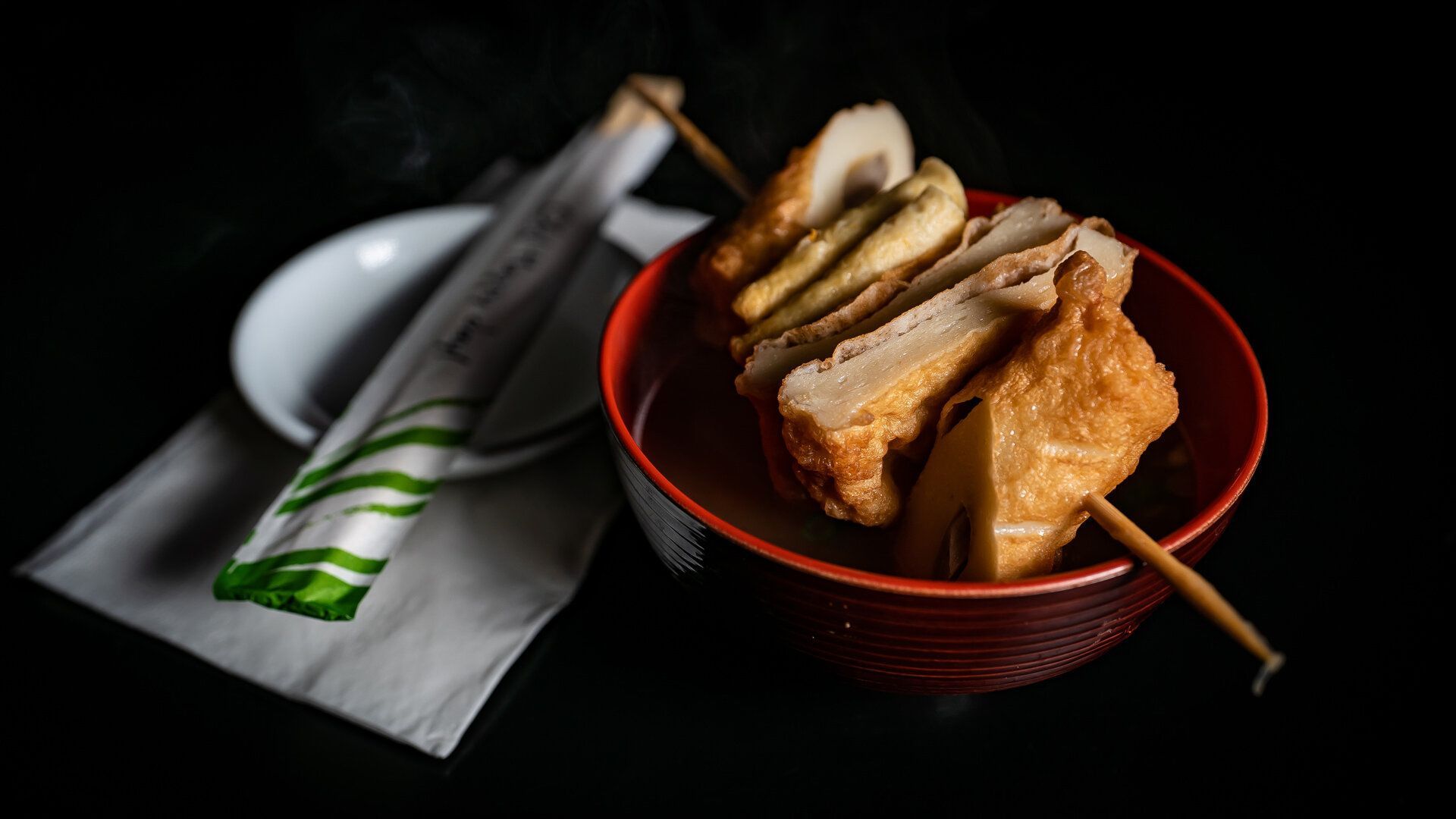 A bowl of food with chopsticks and a plate of food on a table.