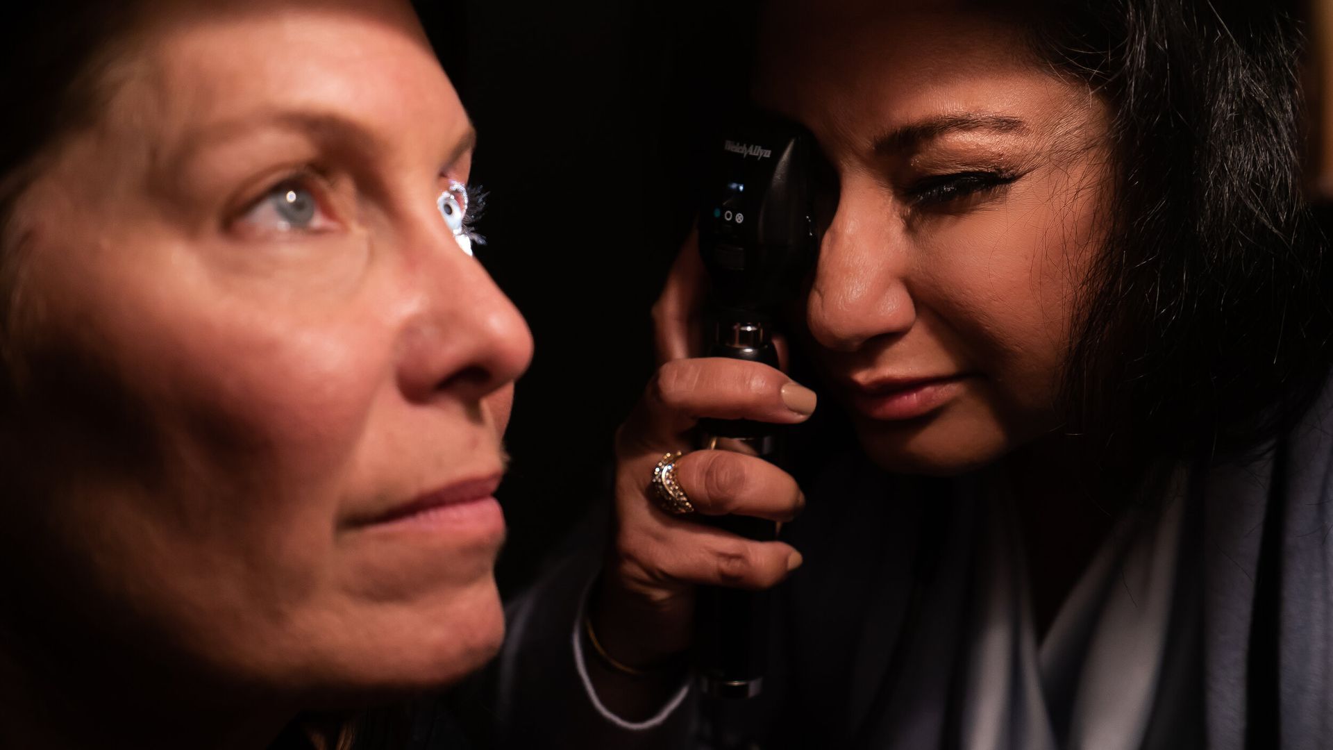A woman is examining another woman 's eye with a magnifying glass.