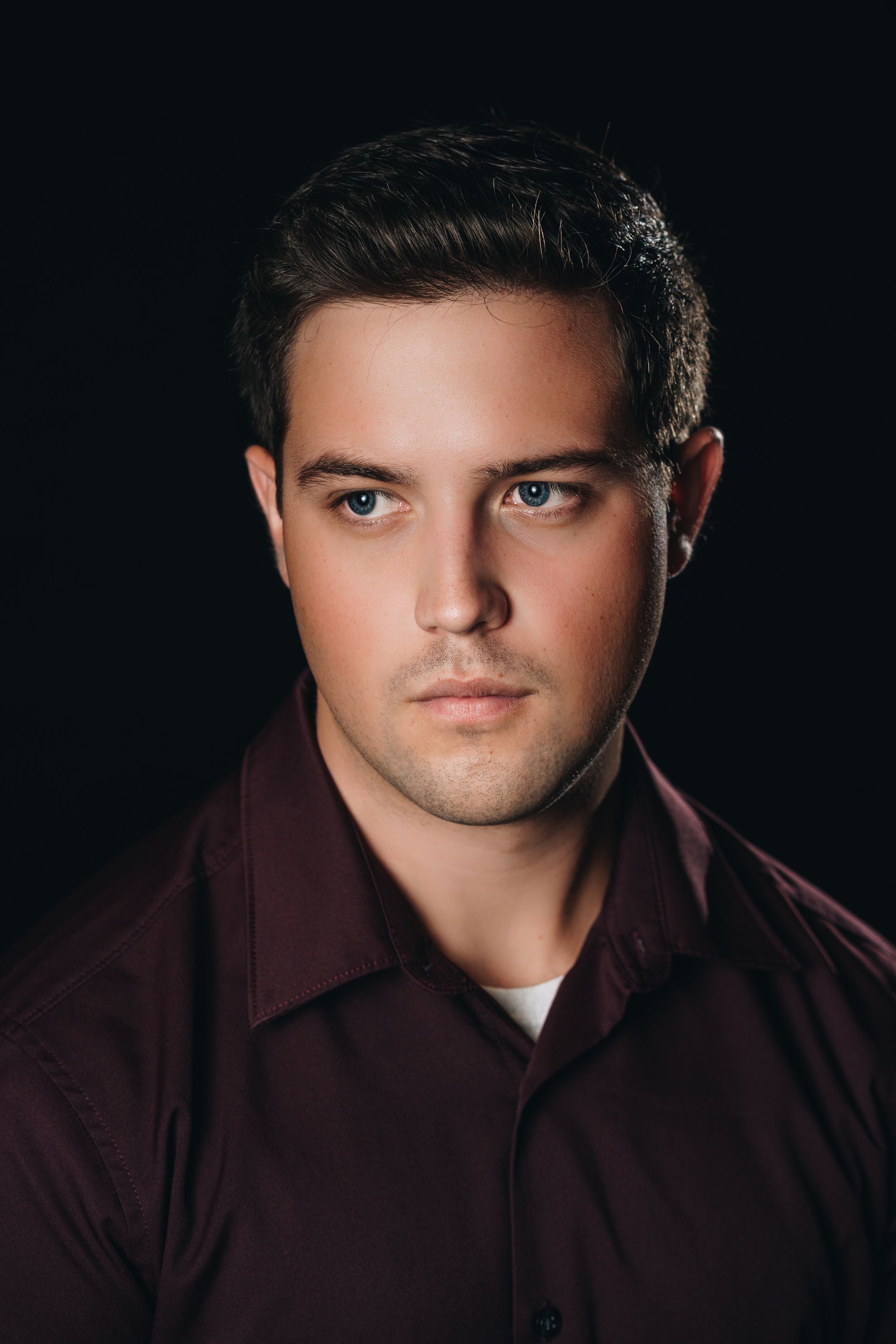 A man in a purple shirt is looking at the camera with a black background.