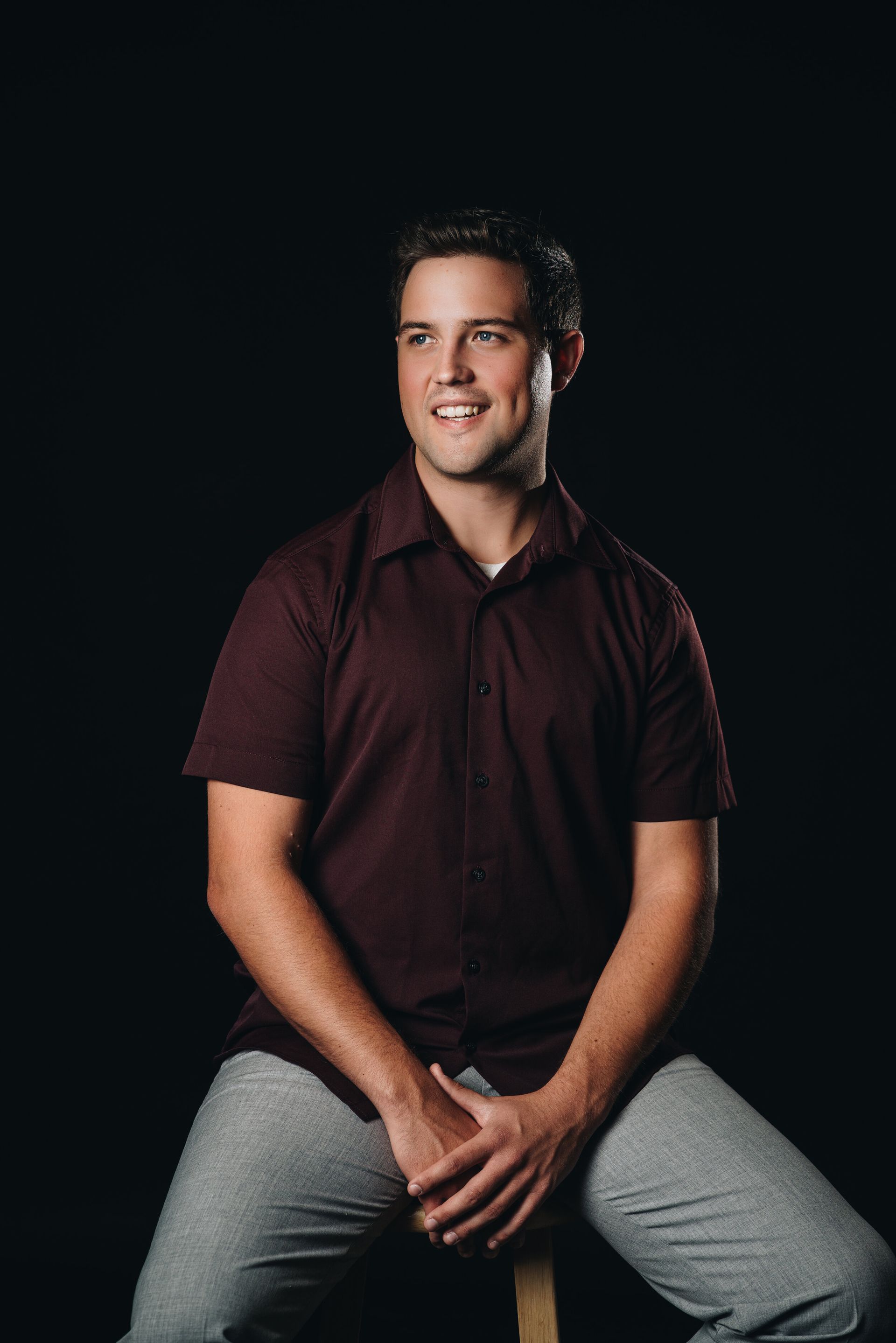 A man in a maroon shirt is sitting on a wooden stool.