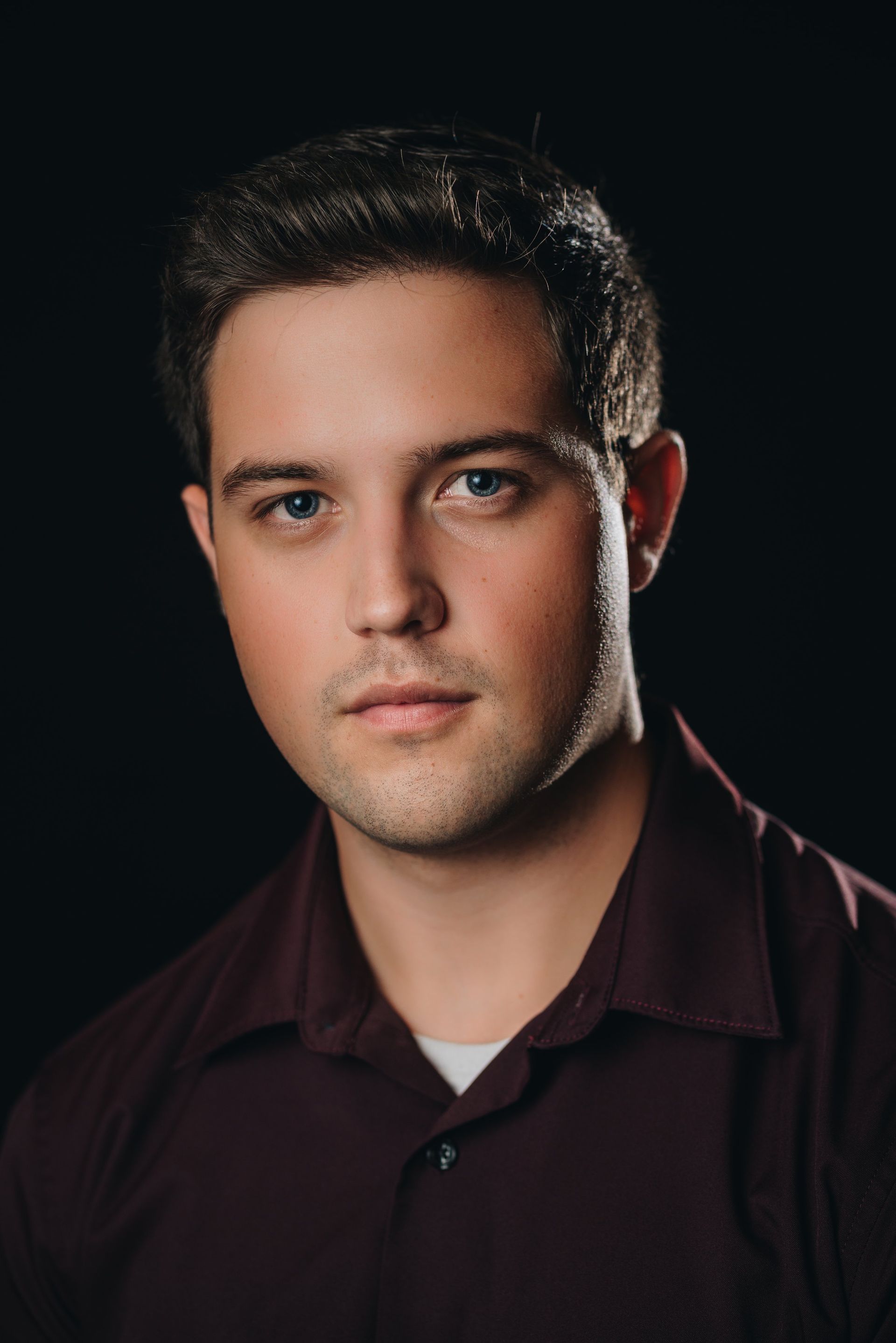 A young man in a purple shirt is looking at the camera.