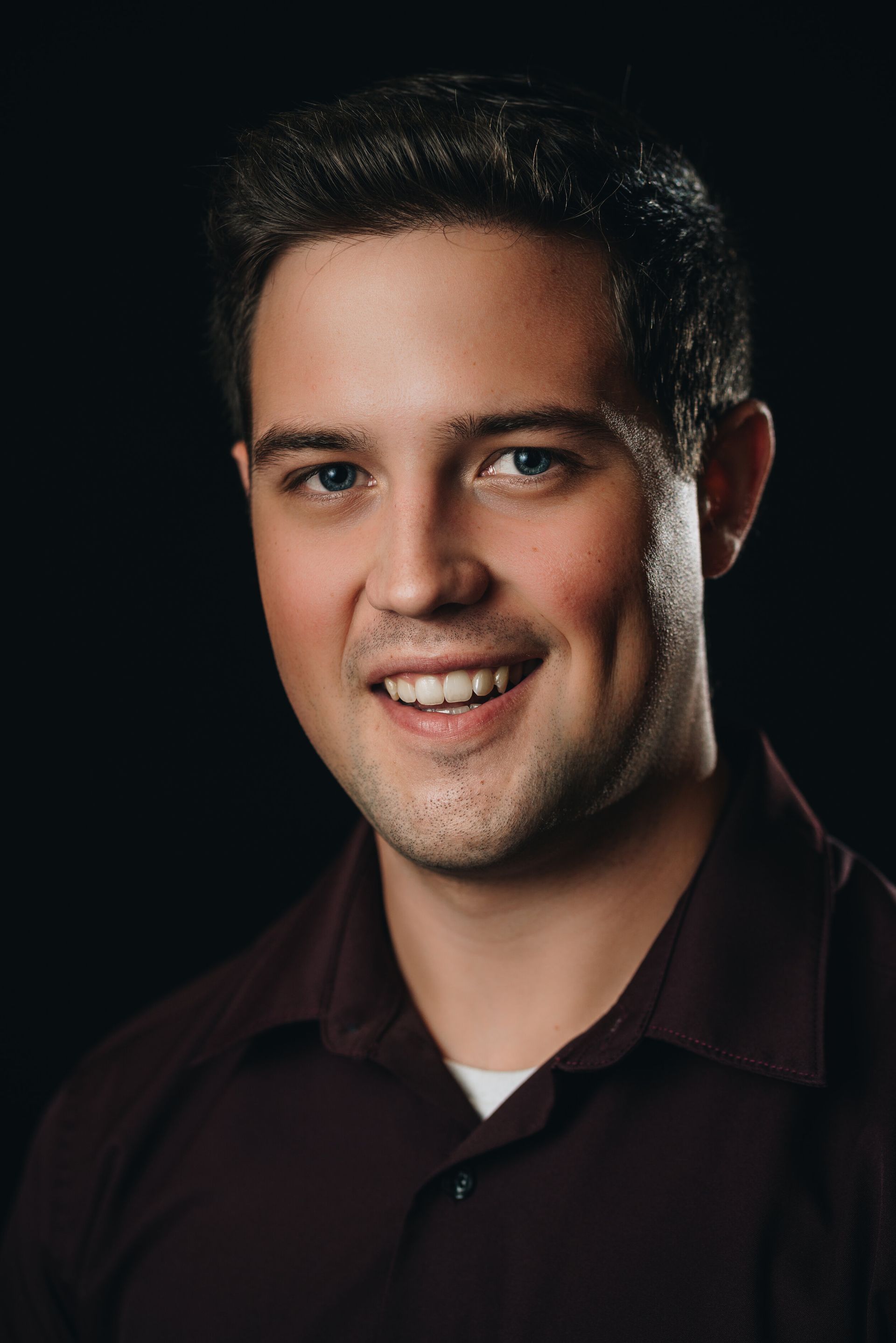 A young man in a maroon shirt is smiling for the camera.