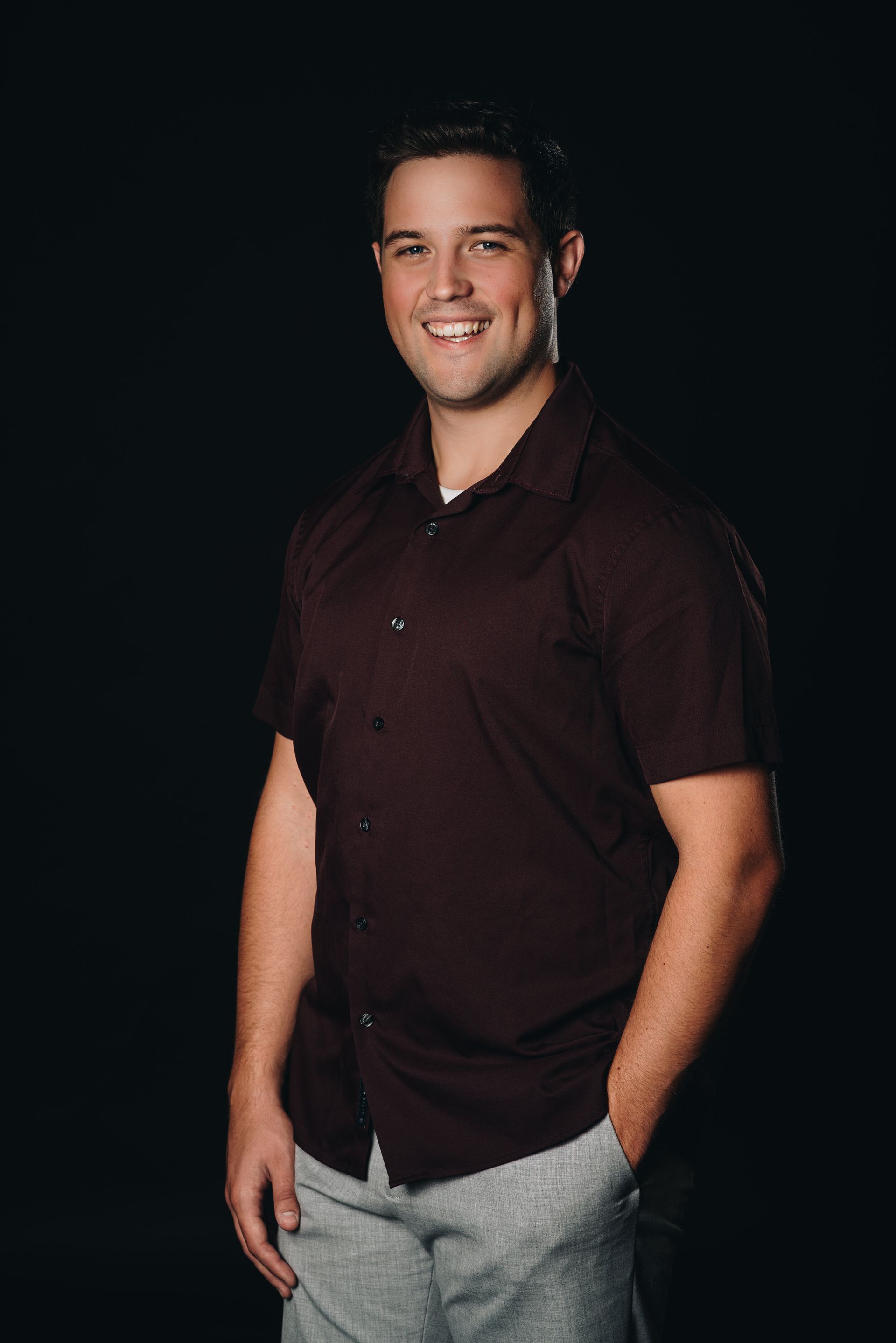 A man in a maroon shirt and grey shorts is standing with his hands in his pockets.