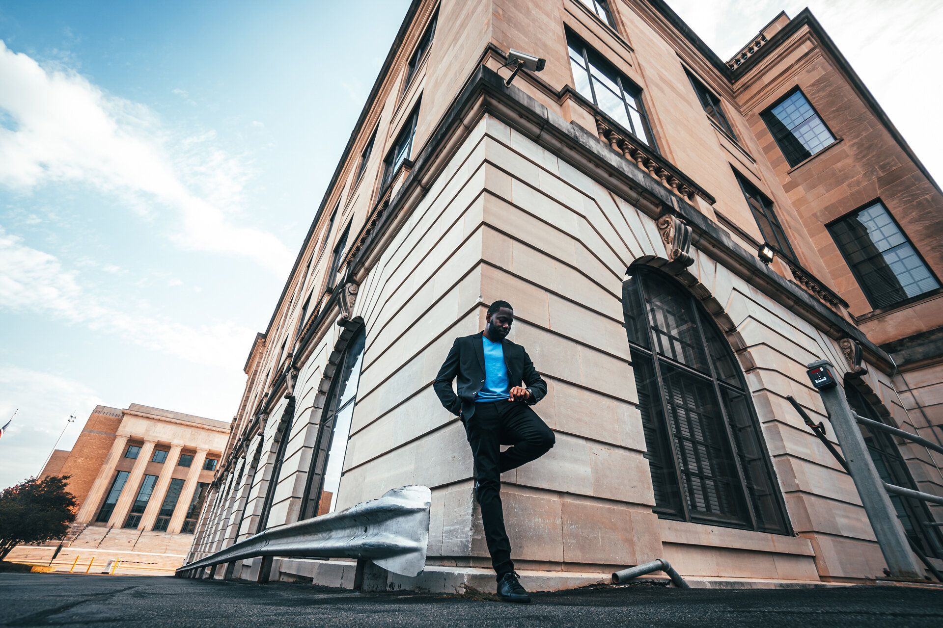 A man in a suit is leaning against the side of a building.