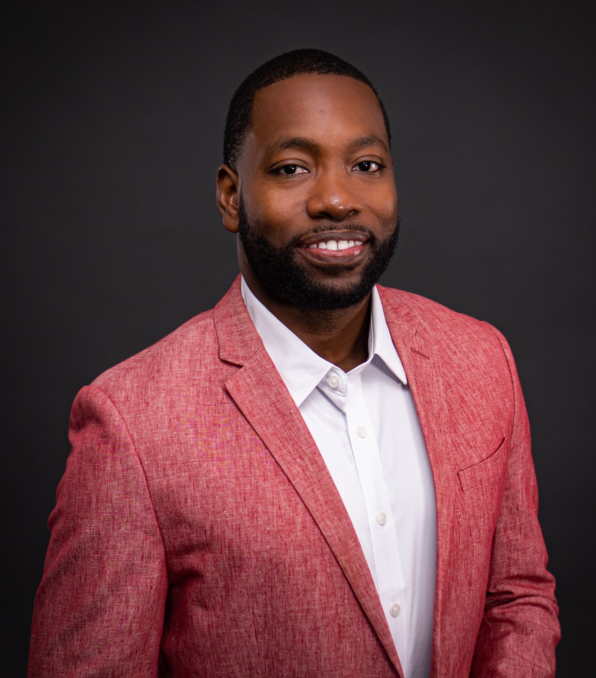 A man with a beard is wearing a red jacket and white shirt.