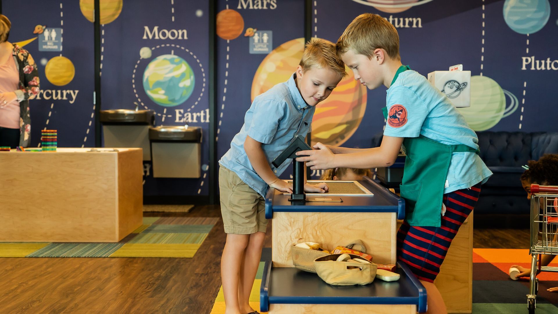 Two young boys are standing next to each other at a table in a room.