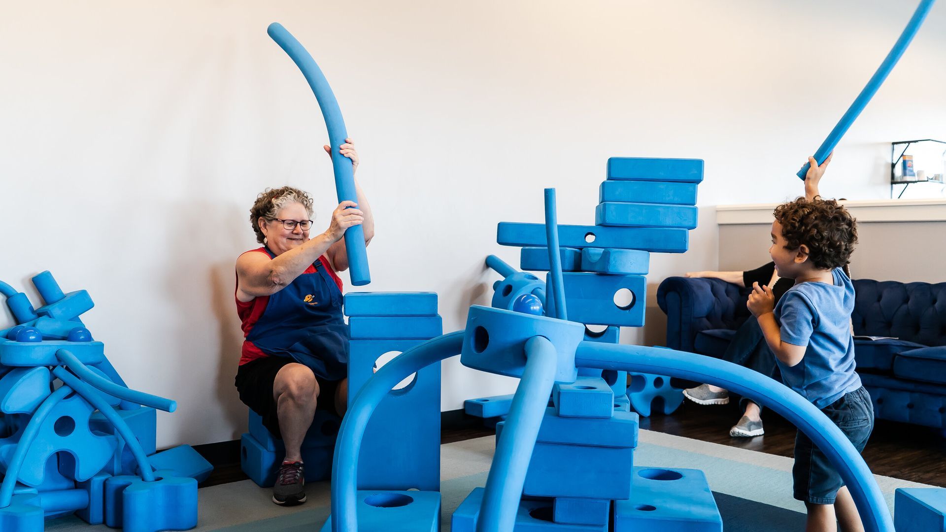 A woman and two children are playing with blue blocks in a room.
