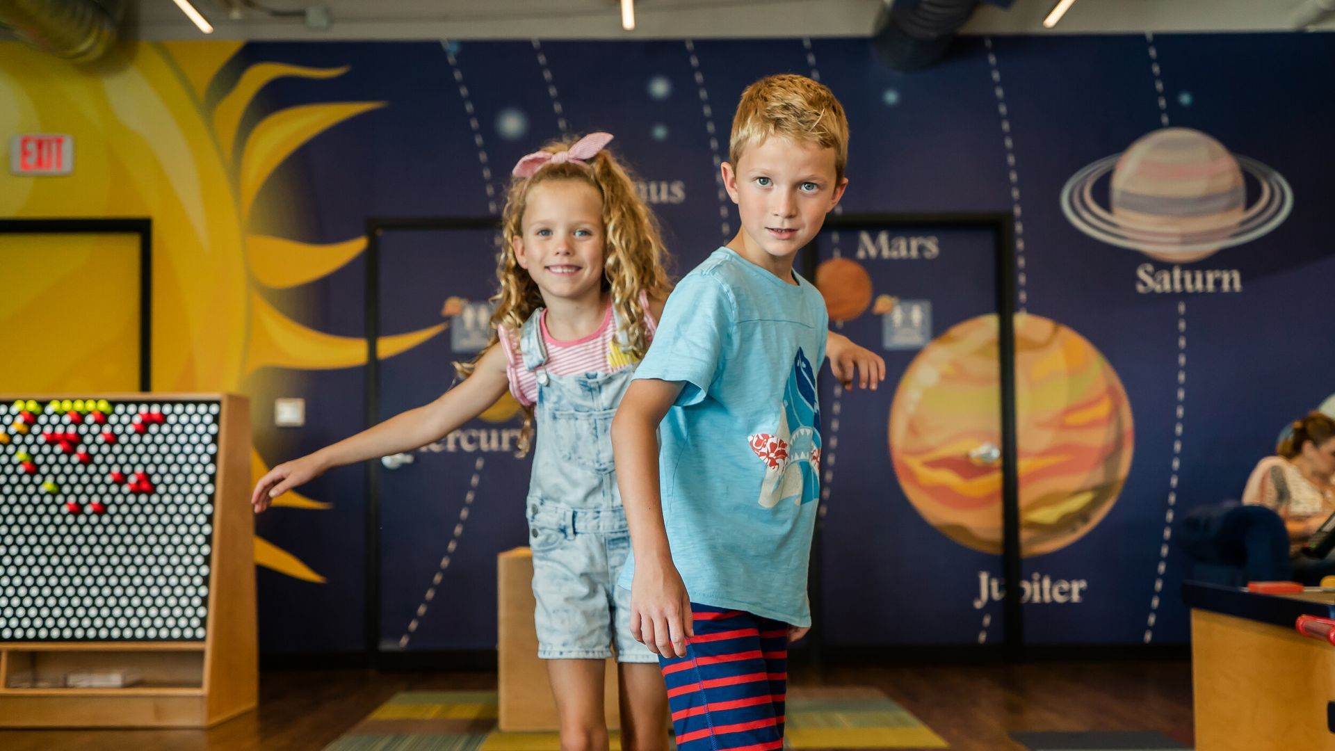 A boy and a girl are standing next to each other in a room with planets on the wall.