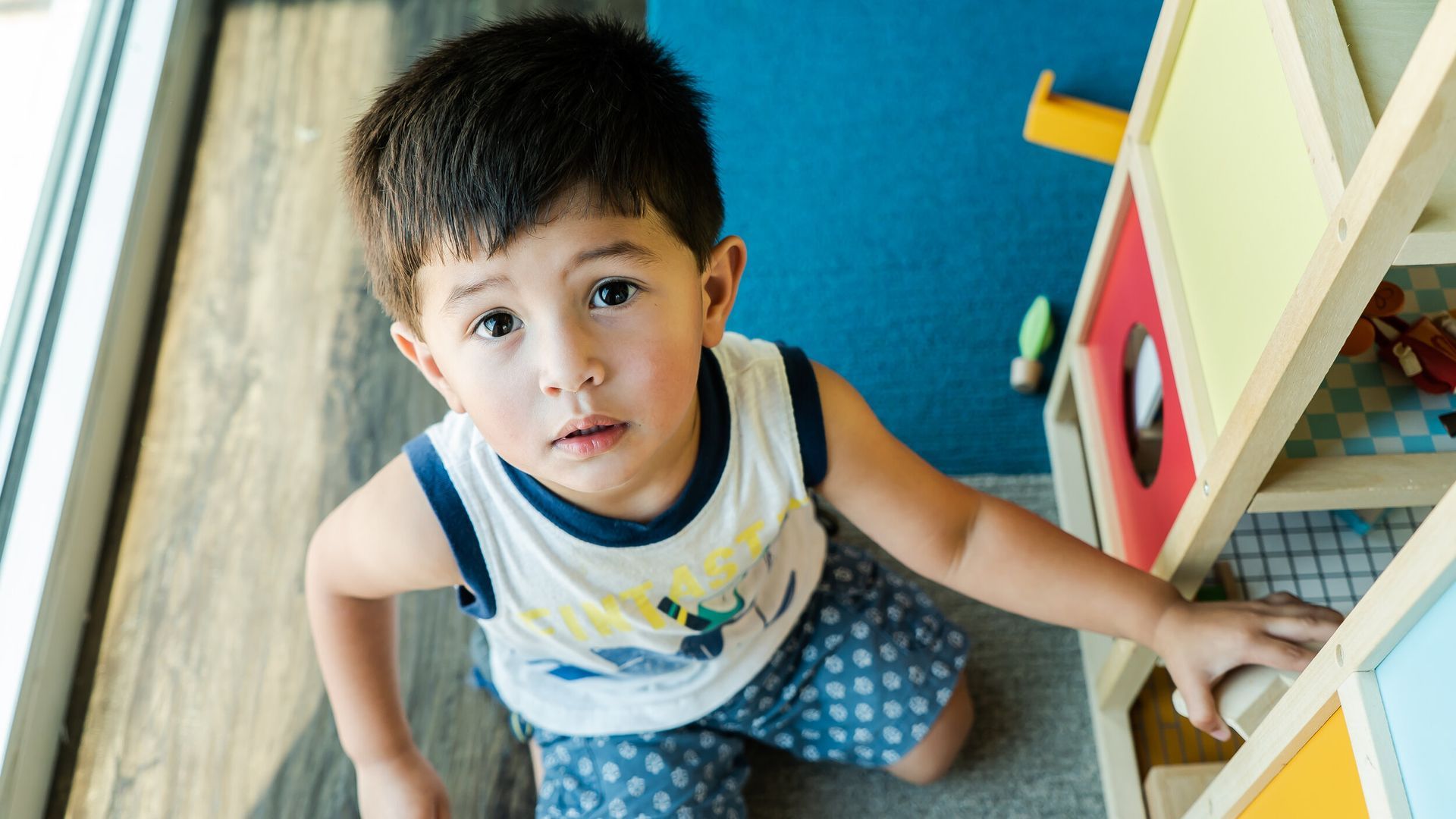 A young boy is playing with a doll house on the floor.