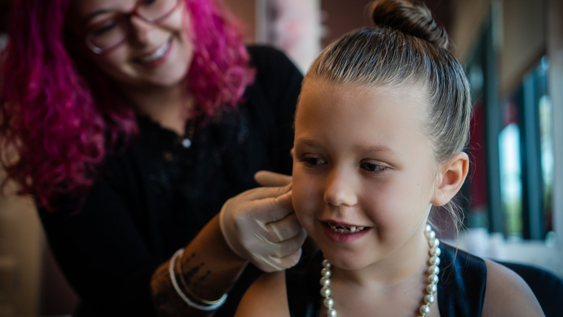 A woman is putting a pearl necklace on a little girl 's ear.