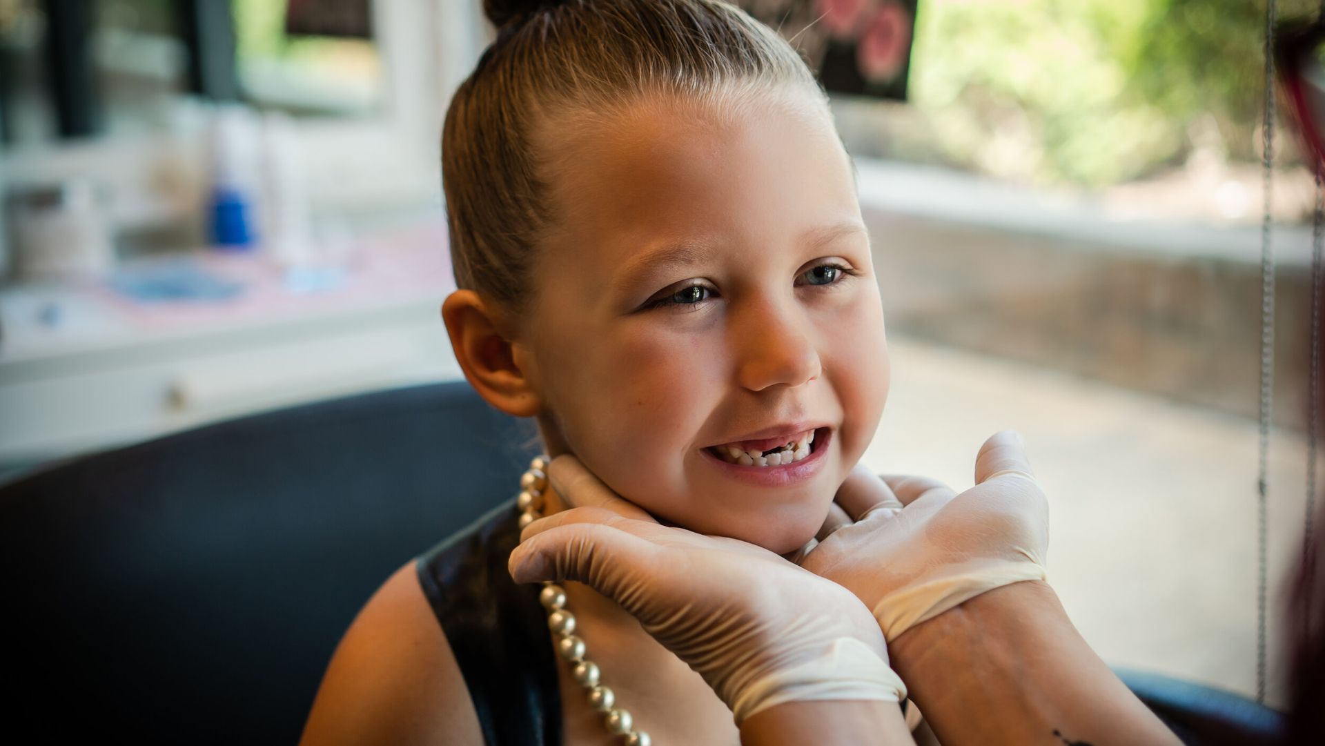A little girl wearing a pearl necklace is getting her ears pierced.