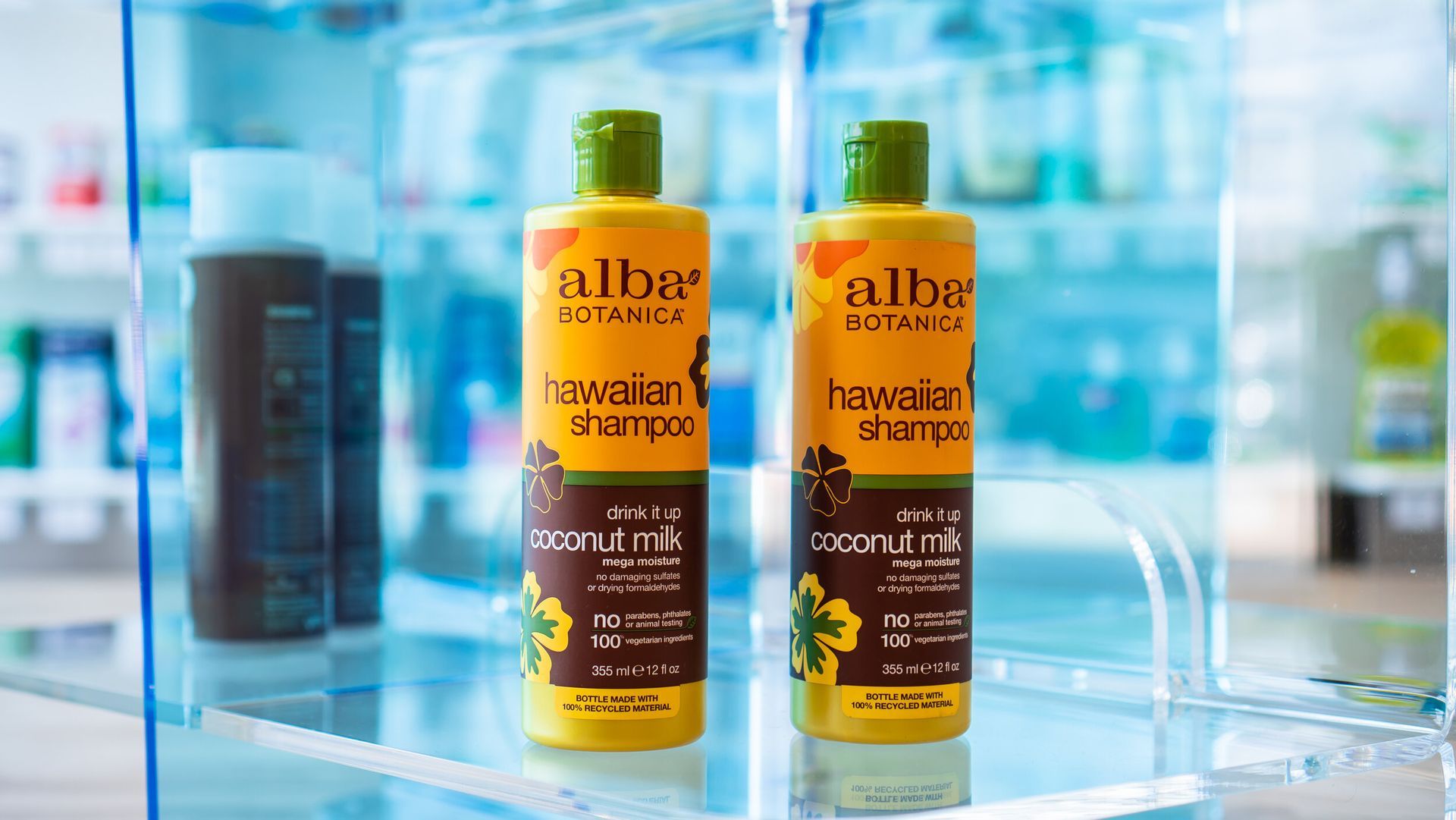 Two bottles of hawaiian shampoo are sitting on a glass shelf.