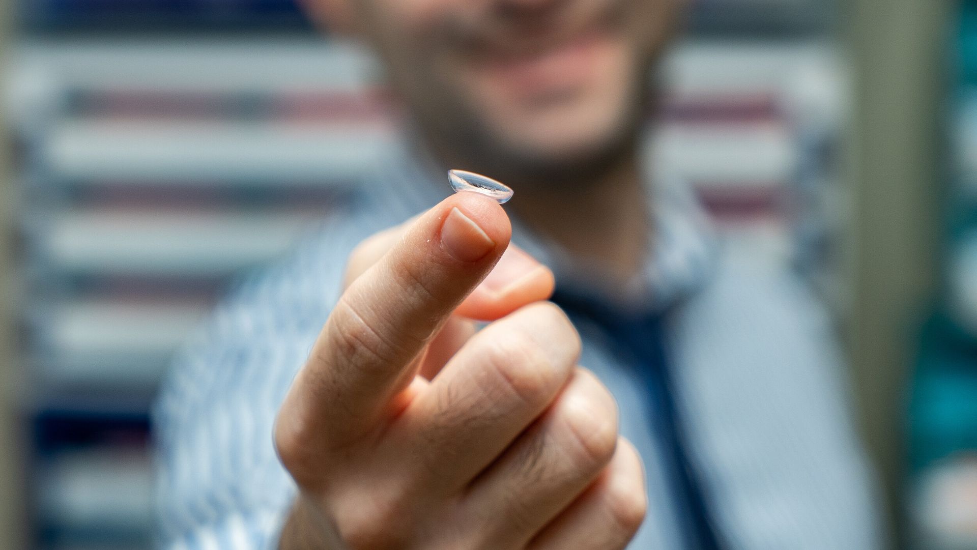 A man is holding a contact lens in his hand.