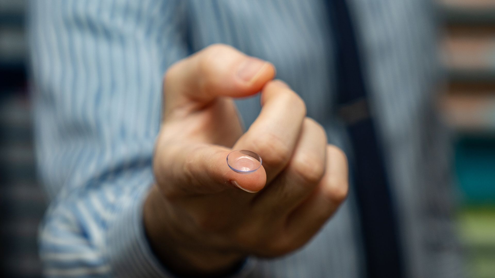A man is holding a contact lens in his hand.