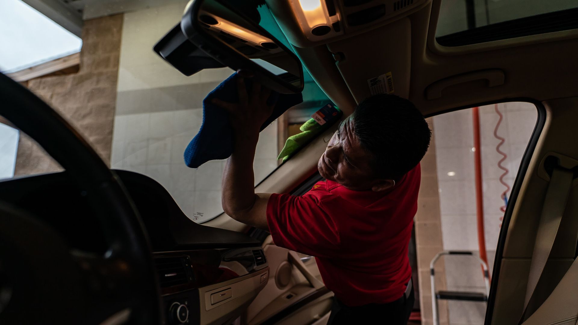 A man in a red shirt is cleaning the windshield of a car.