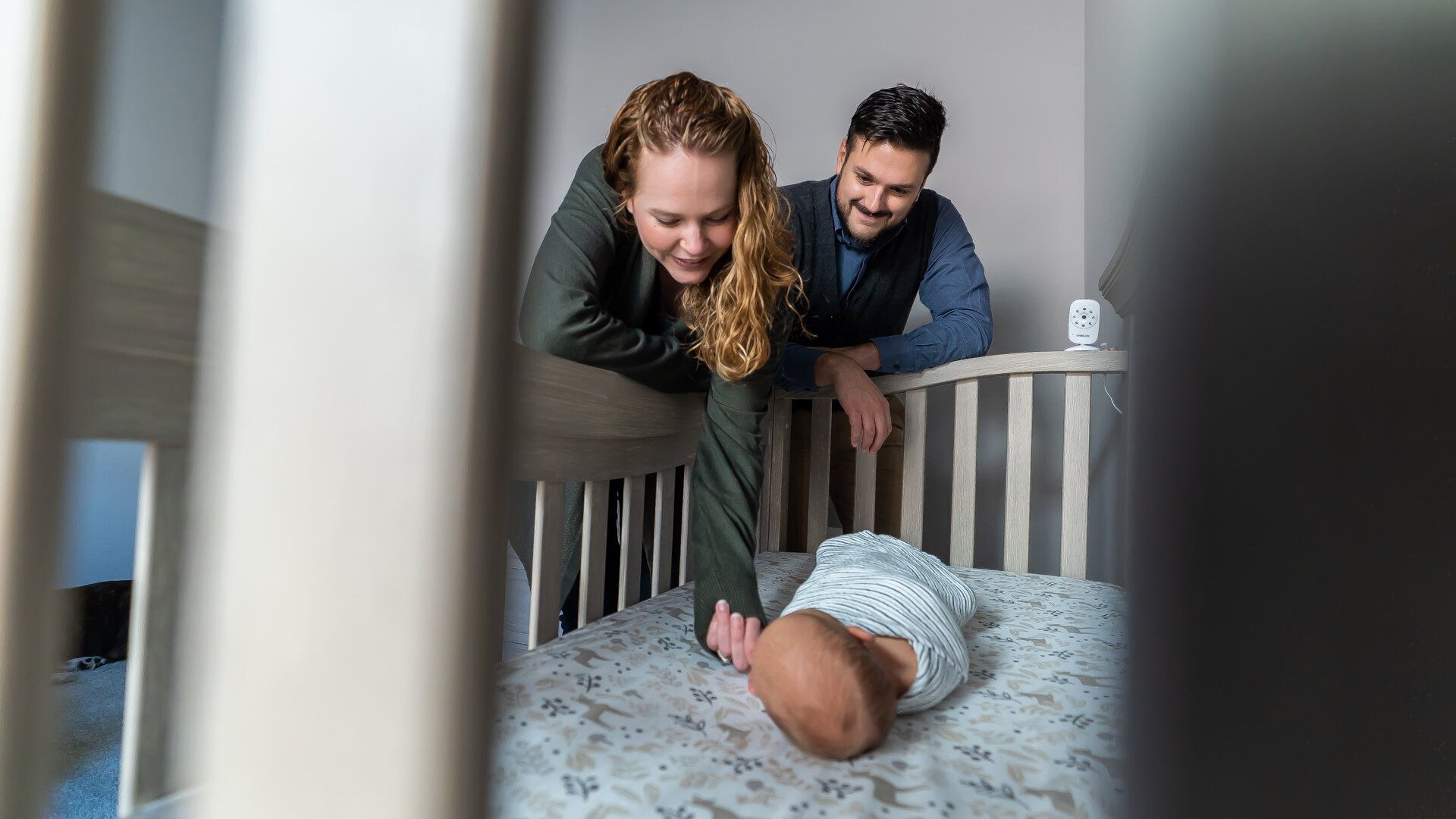 A man and a woman are looking at a baby in a crib.