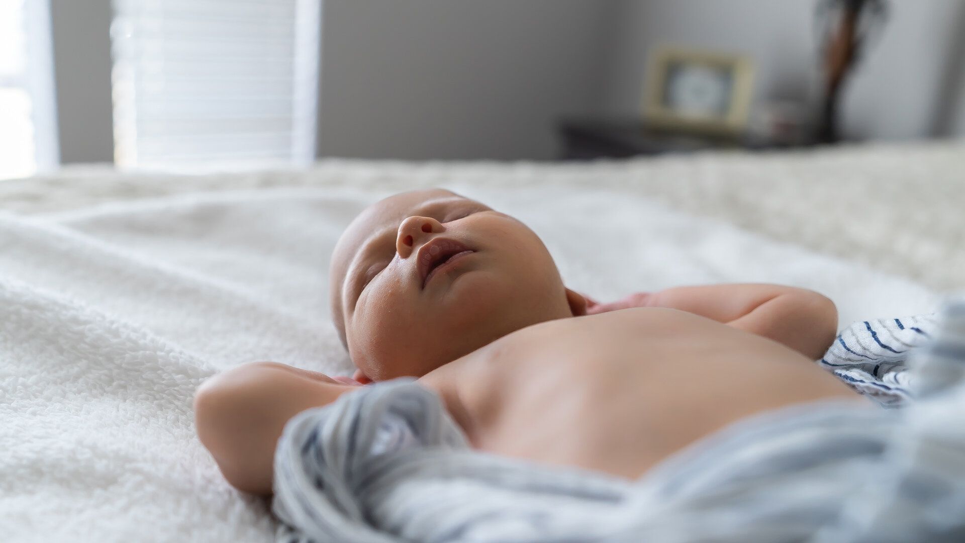 A newborn baby is sleeping on a bed without a shirt on.