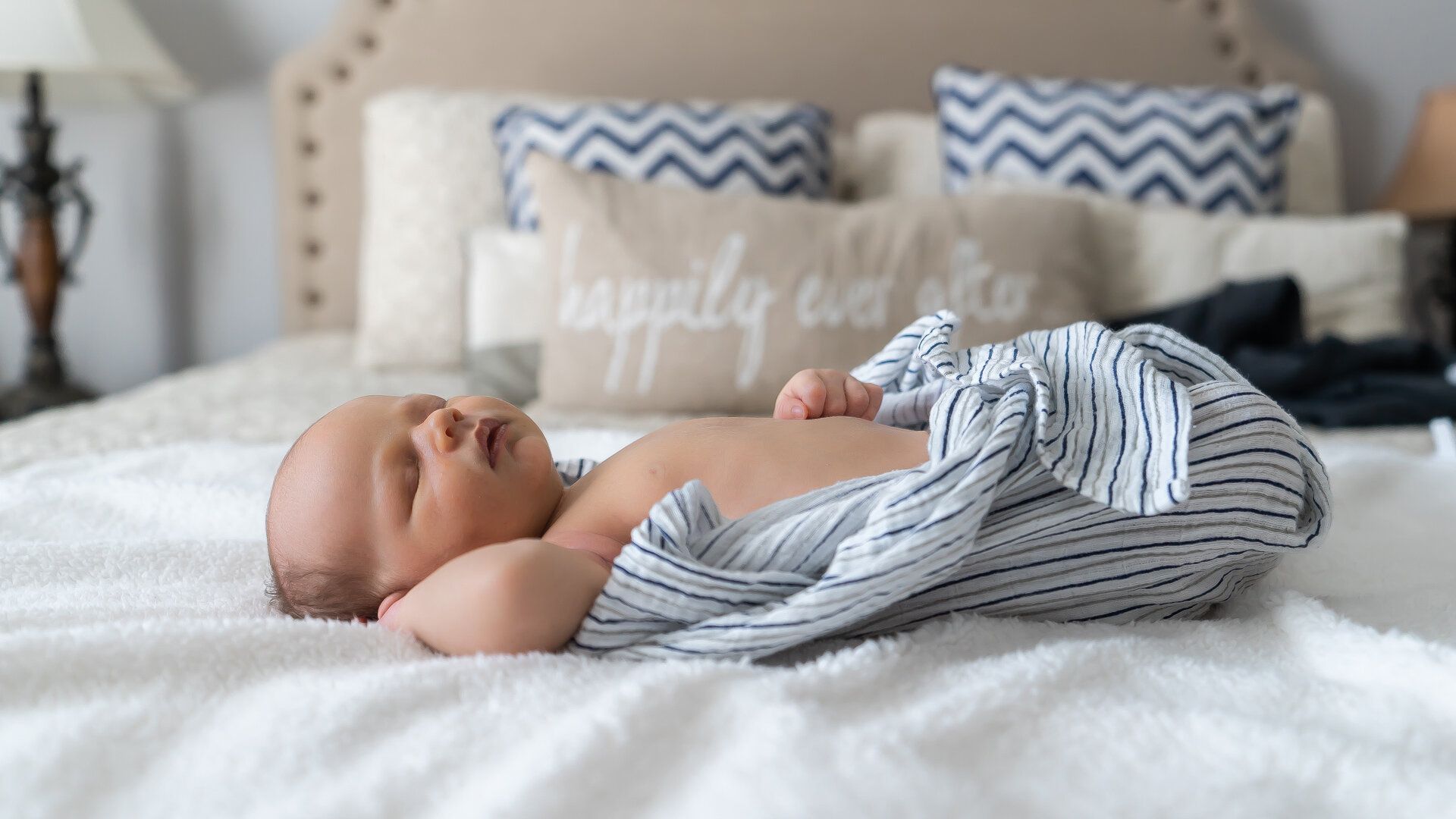 A newborn baby wrapped in a striped blanket is laying on a bed.