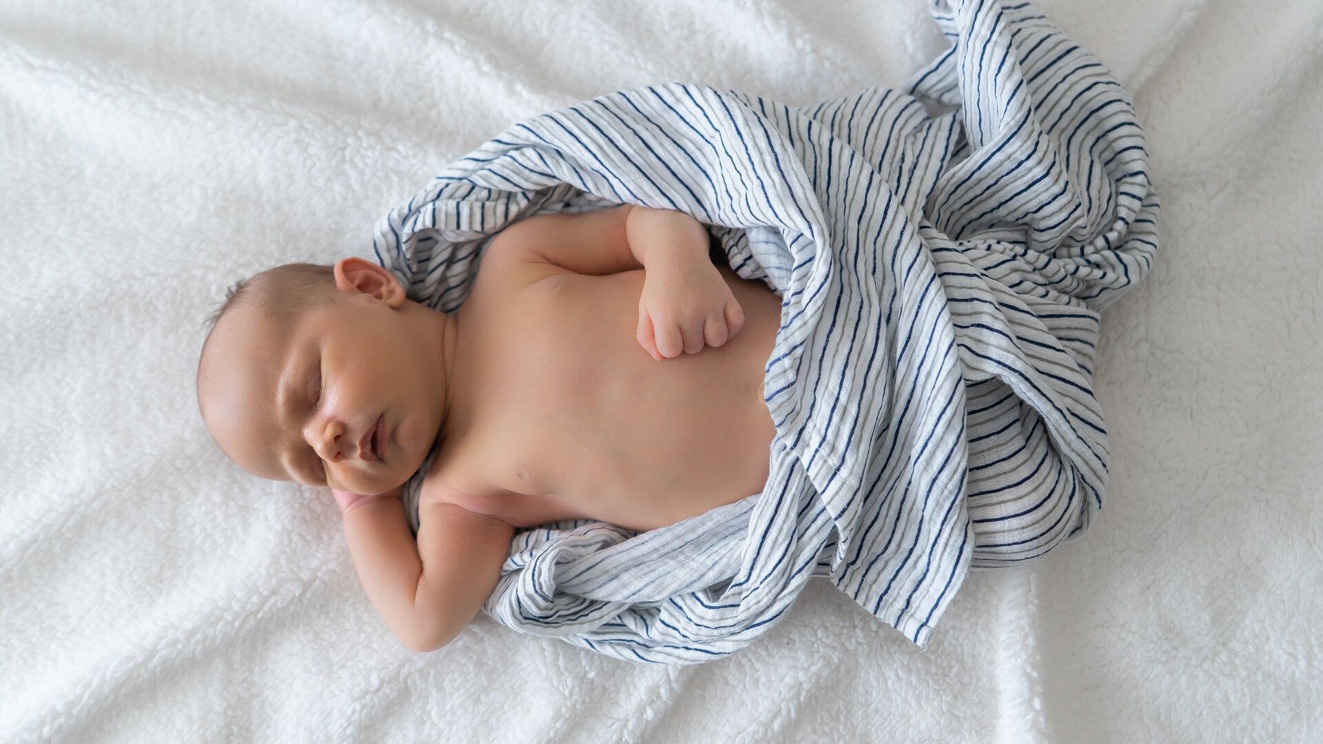 A newborn baby wrapped in a blanket is sleeping on a bed.