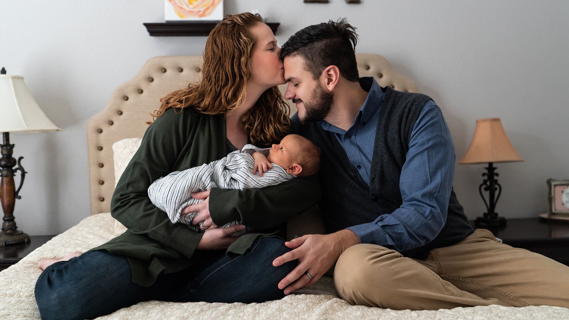 A man and woman are sitting on a bed with a newborn baby.