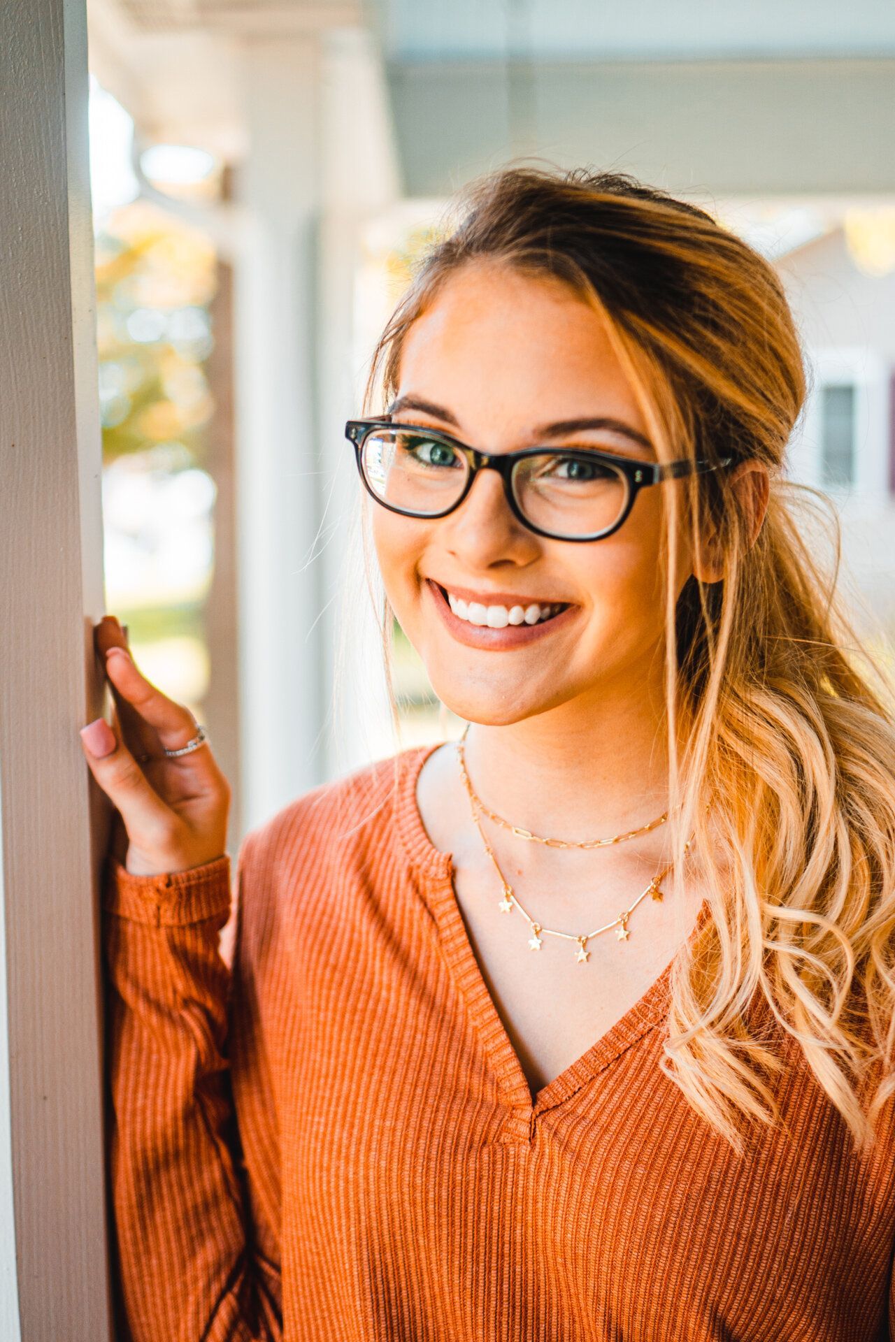 A woman wearing glasses and an orange sweater is smiling.