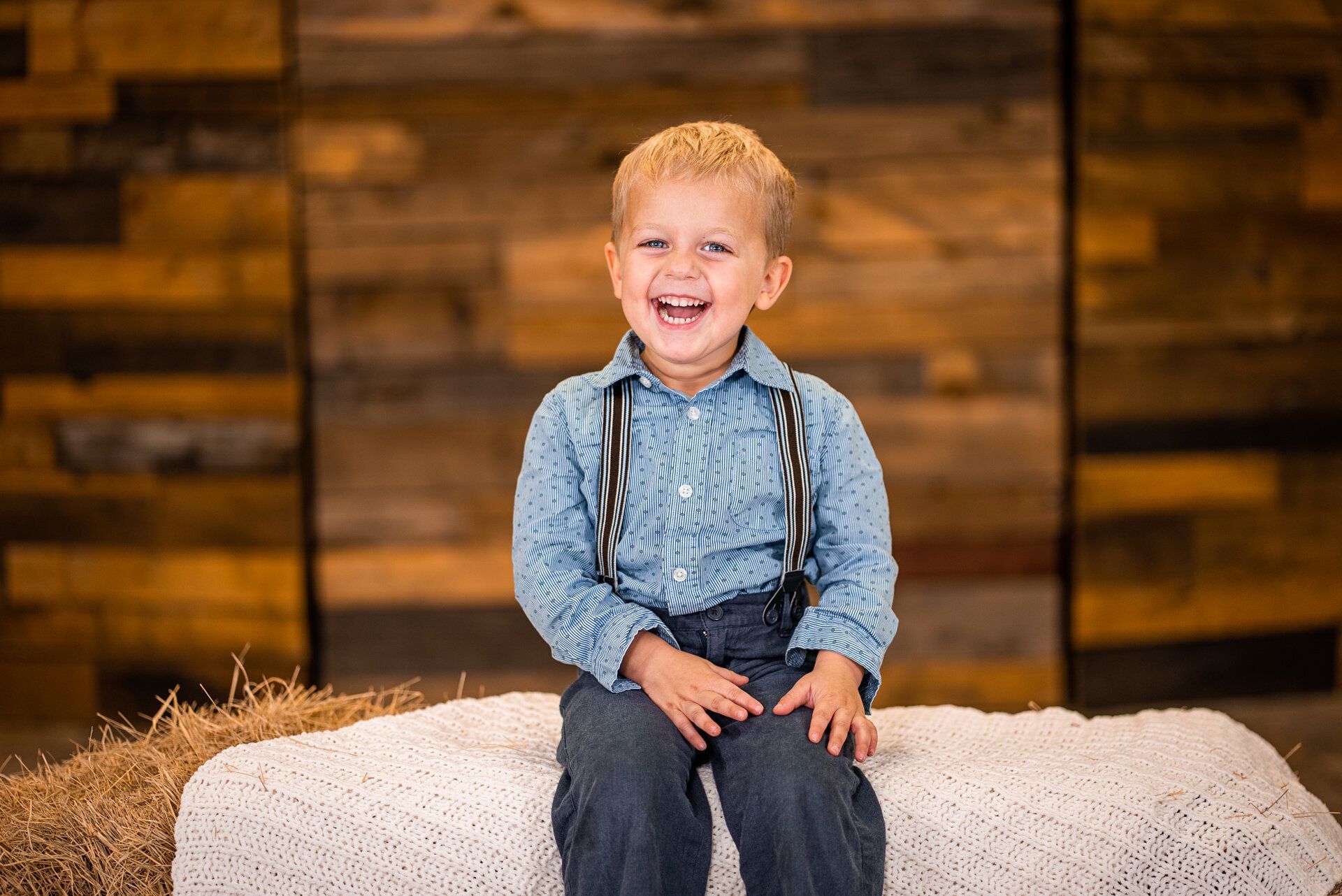 A young boy is sitting on a bale of hay and smiling.