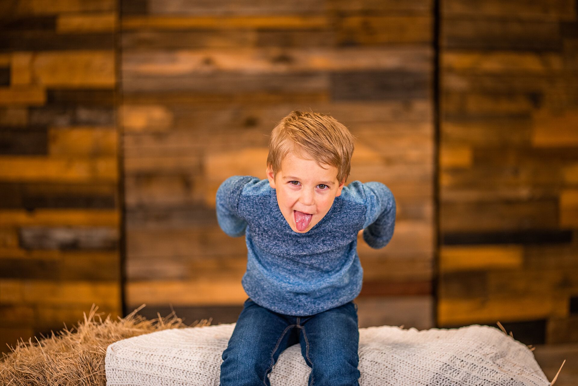 A young boy is sitting on a bale of hay making a funny face.