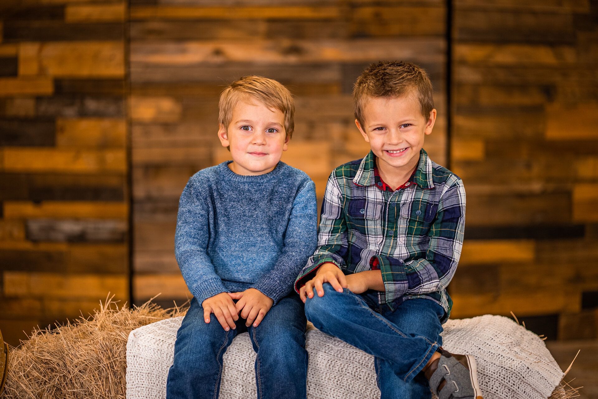 Two young boys are sitting next to each other on a bale of hay.