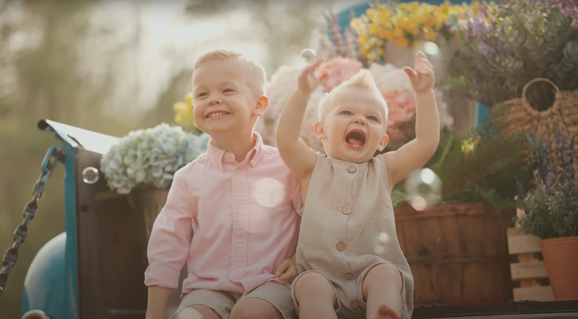 Two little boys are sitting in the back of a truck.