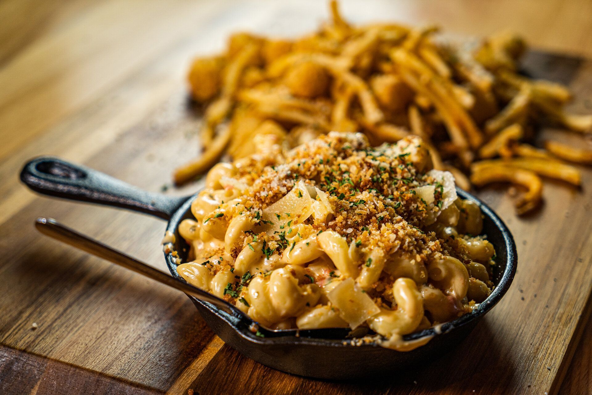 A skillet filled with macaroni and cheese and french fries on a wooden table.