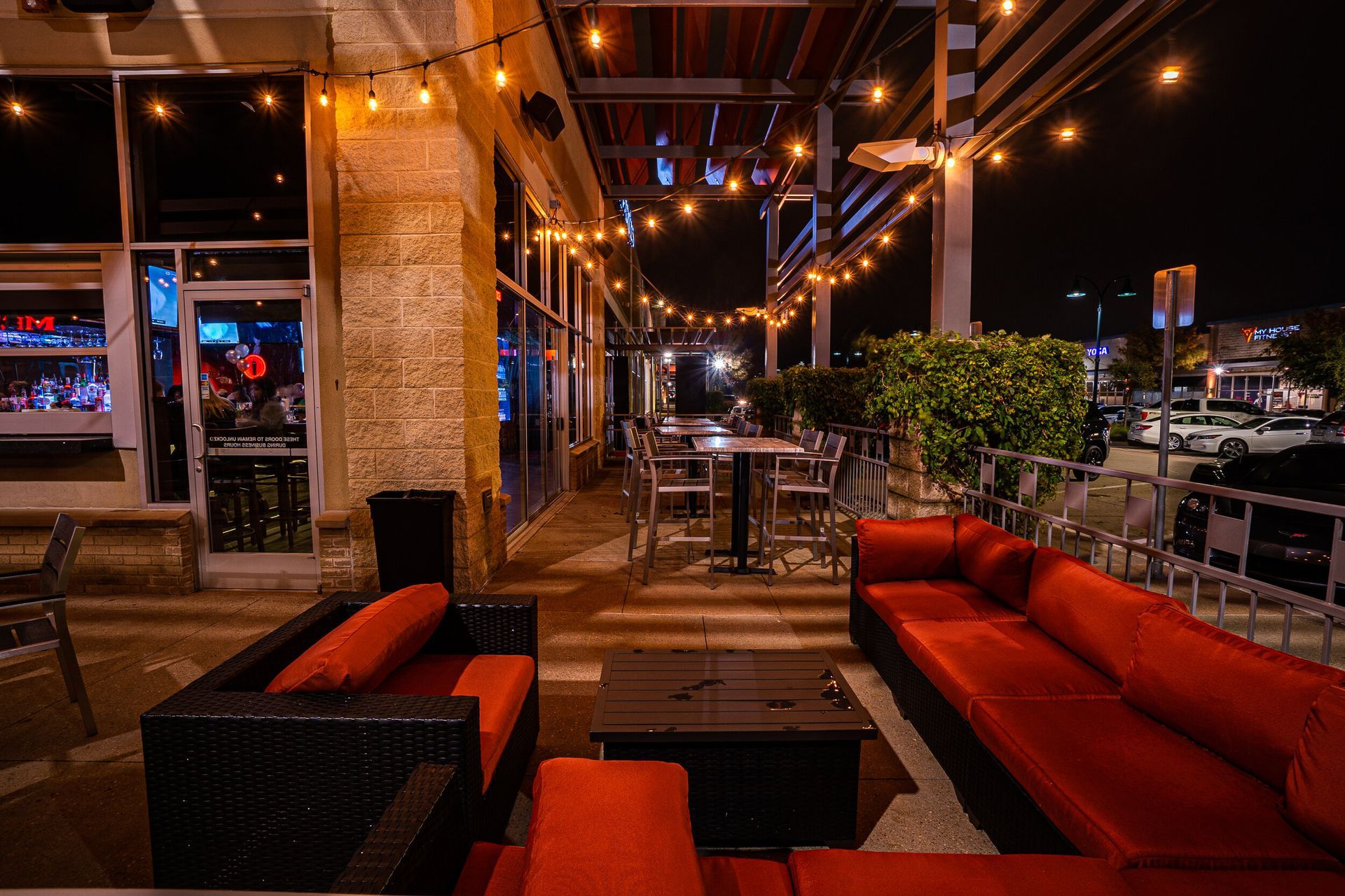 A patio area with a couch , chairs , and tables at night.