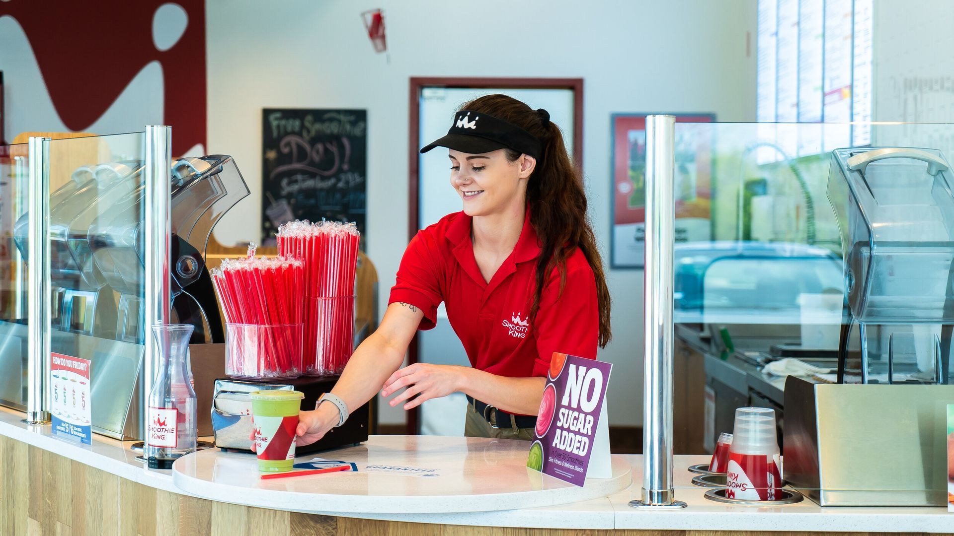 A woman in a red shirt is standing behind a counter in a restaurant.