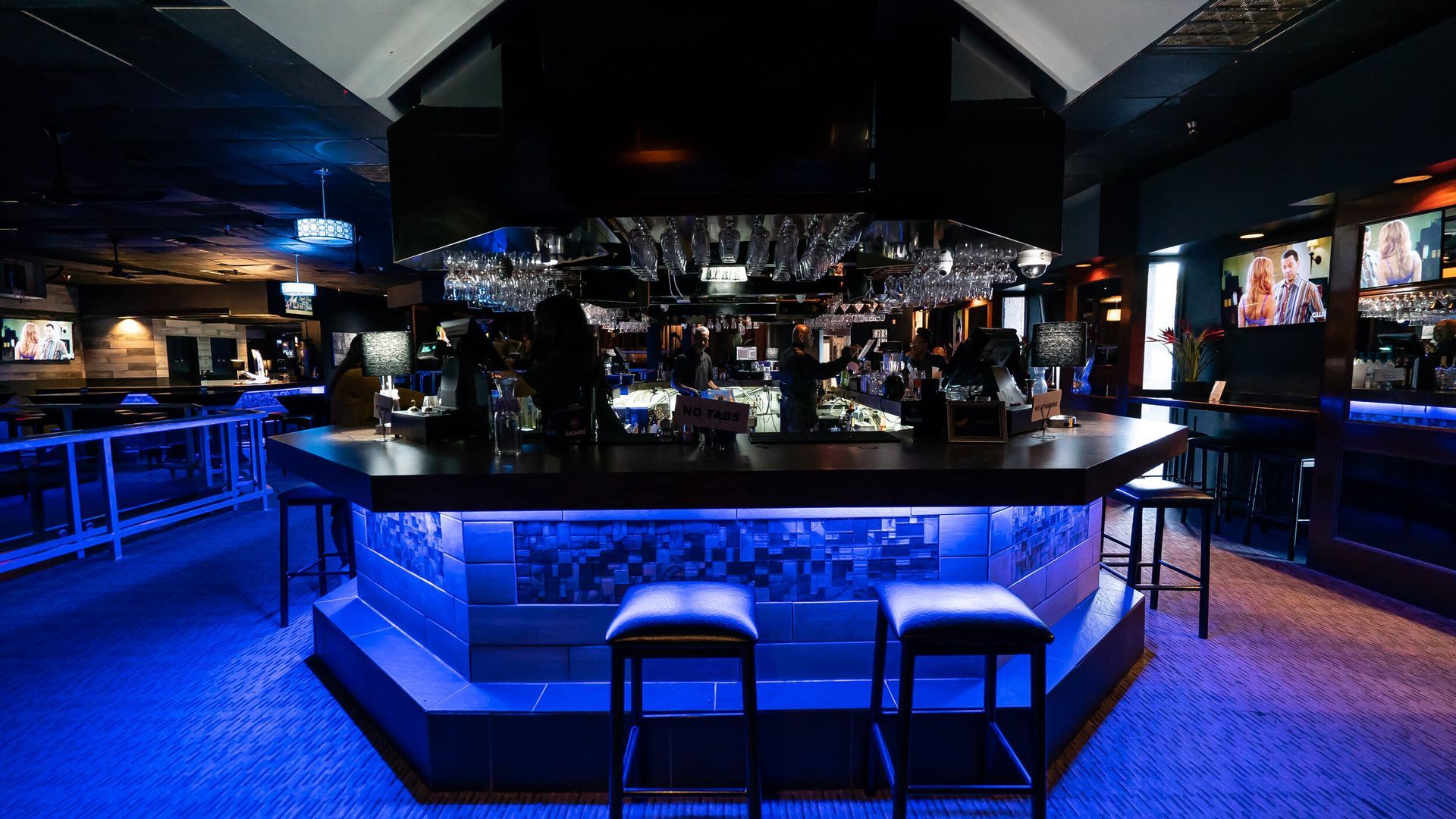 A bar with blue lights and stools in a dark room.